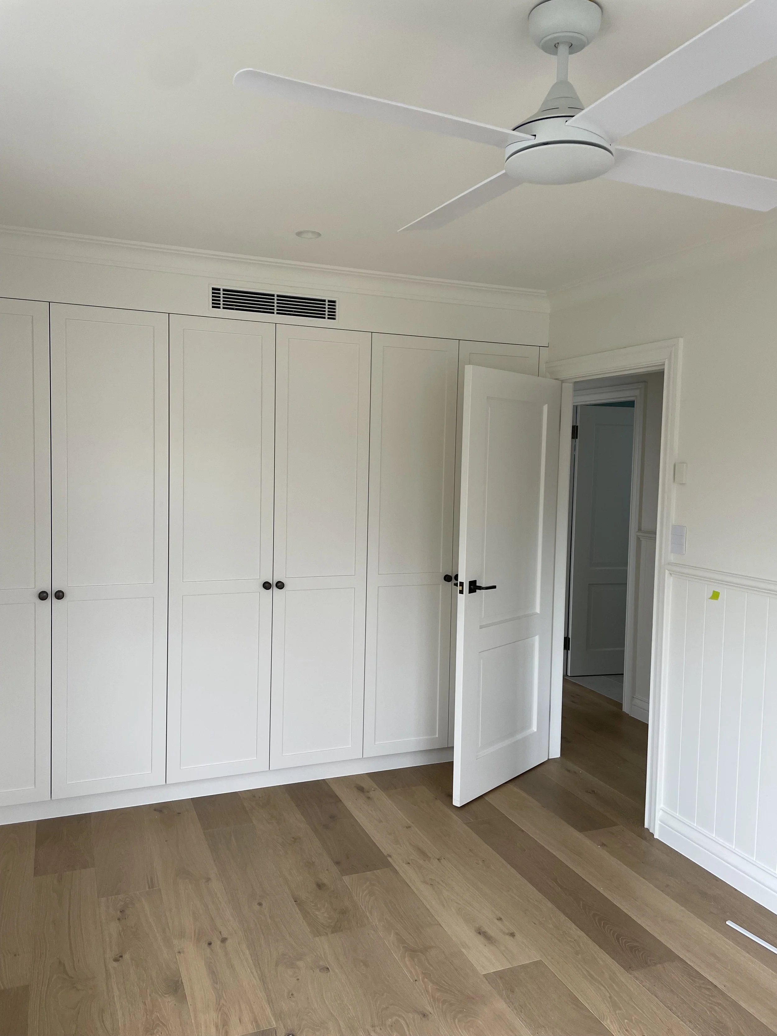 Empty room with white built-in closet, open door, hardwood flooring, ceiling fan, and air vent.