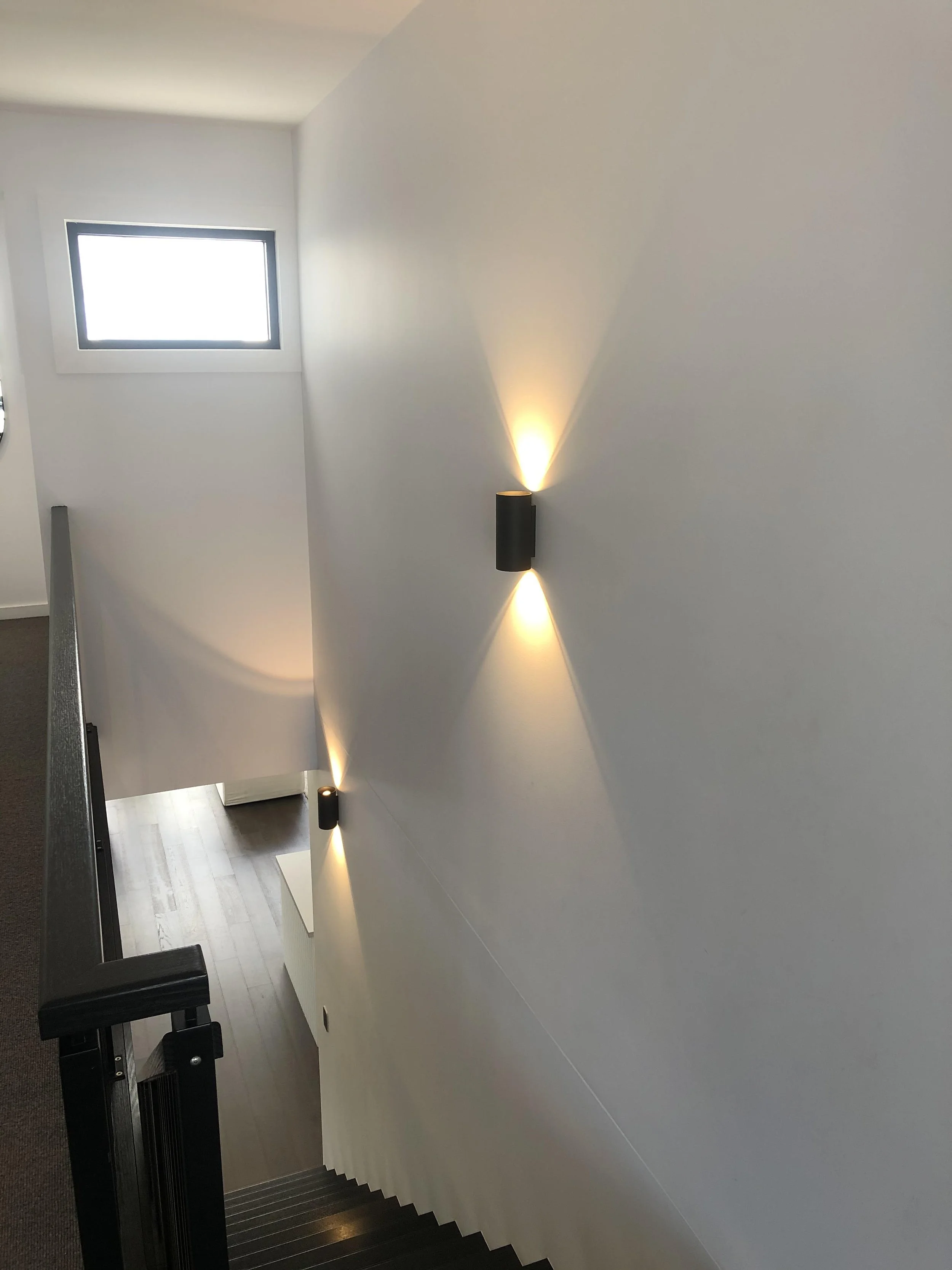 Photo of a staircase with modern black wall-mounted lights illuminating the white wall.