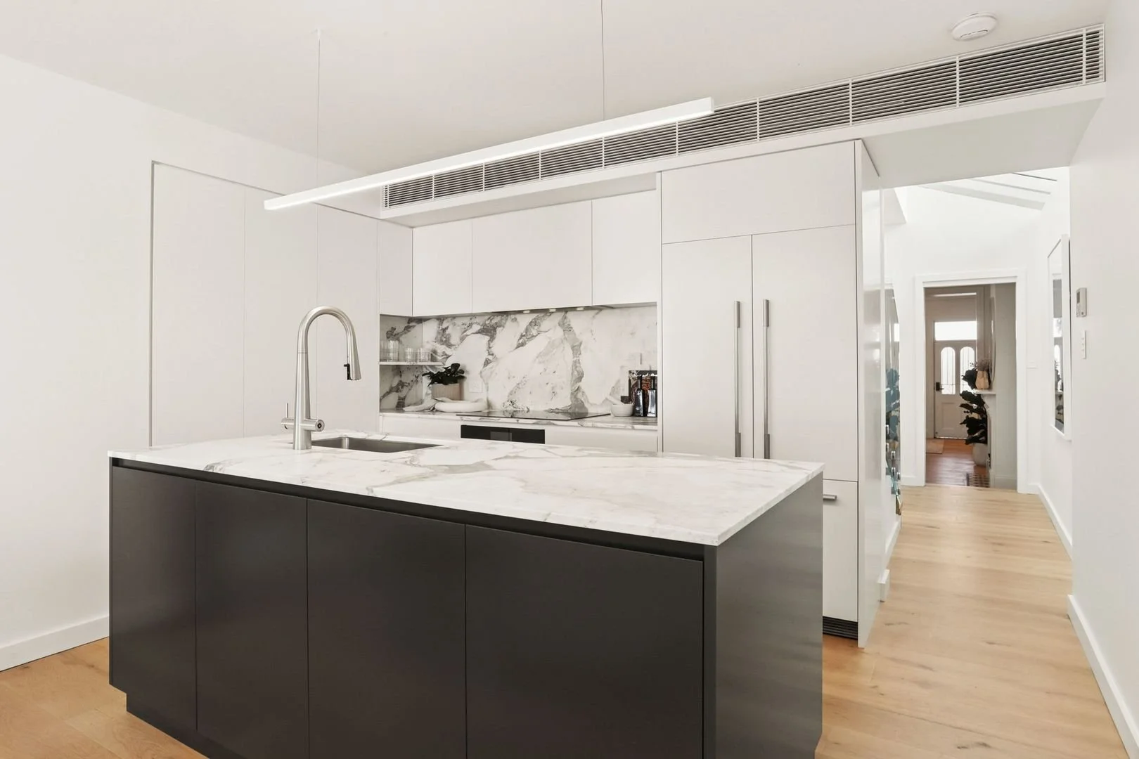 Modern kitchen with white cabinets, marble backsplash, black kitchen island, stainless steel faucet, and light wood flooring.
