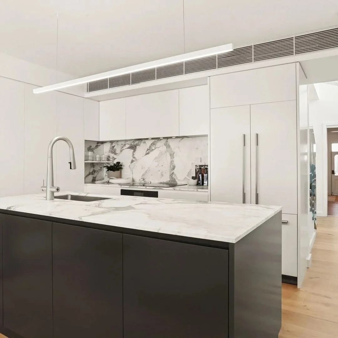Modern kitchen with white cabinetry, marble backsplash, and a marble countertop island with a sink.