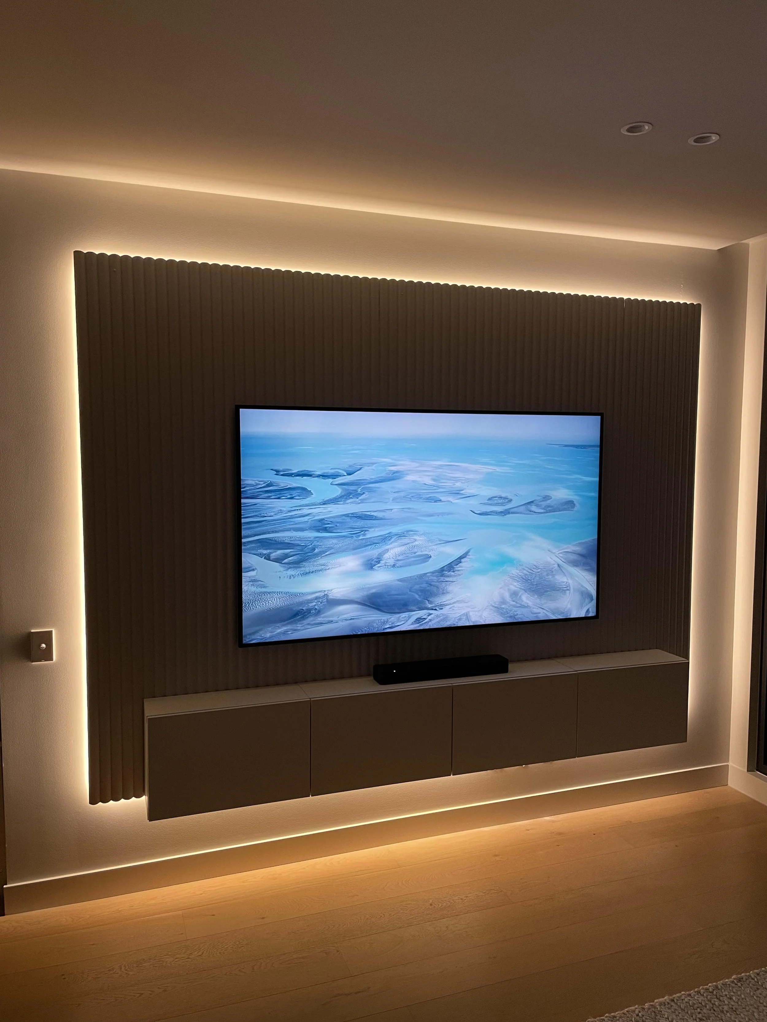 Modern living room with a wall-mounted flat-screen TV displaying an aerial view of snow-covered landscapes, with ambient lighting behind for a cozy atmosphere.