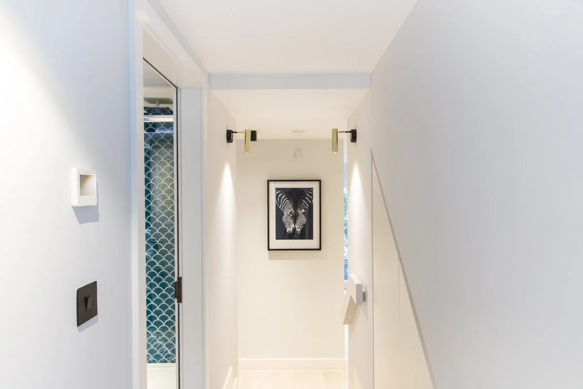 Corridor with zebra wall hung print, side lighting and glimpse of blue mosaic tiles of bathroom