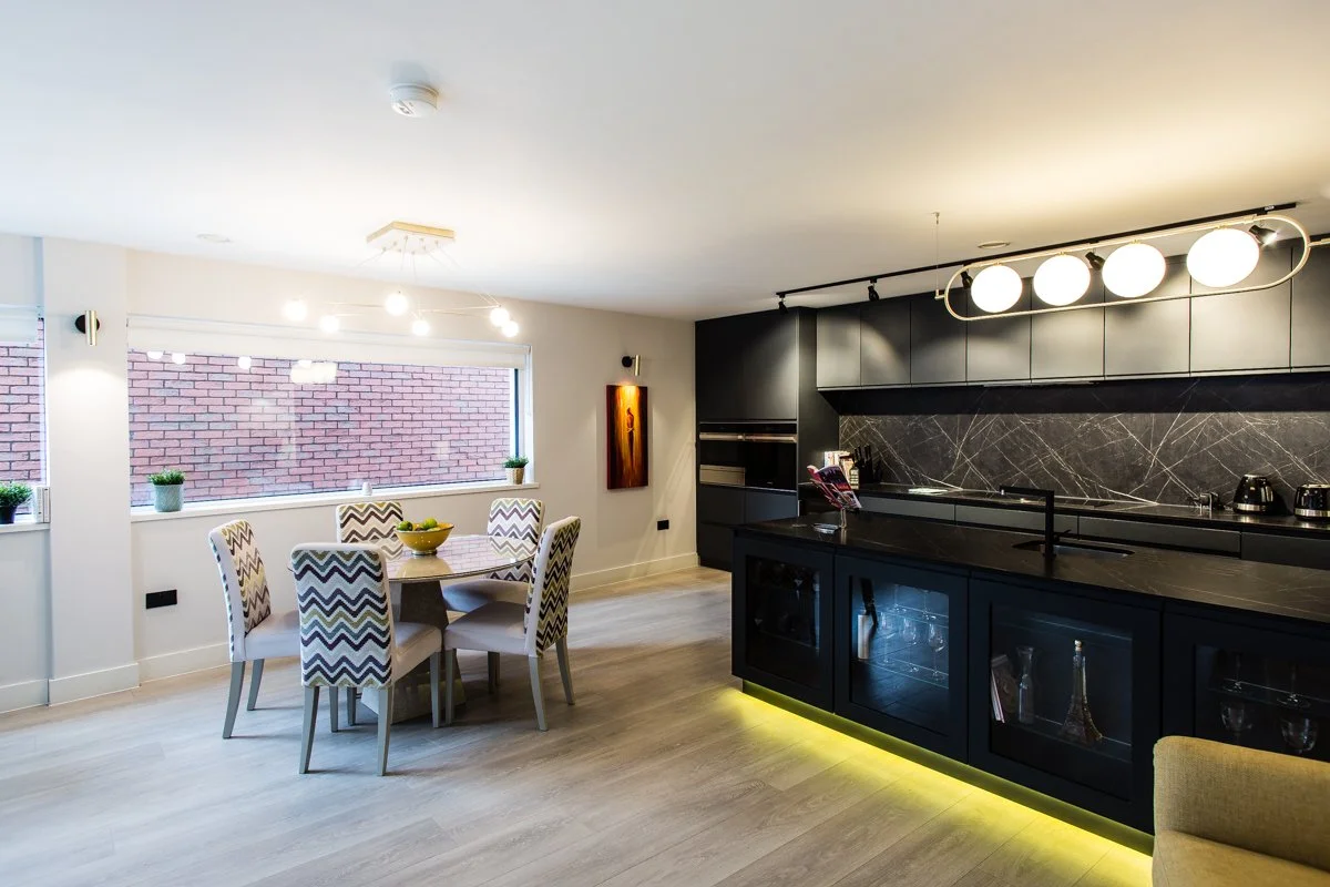 Sleek kitchen with large kitchen island, wine fridge, mustard velvet chair, marble dining table and chairs, and artwork with overhead lighting.