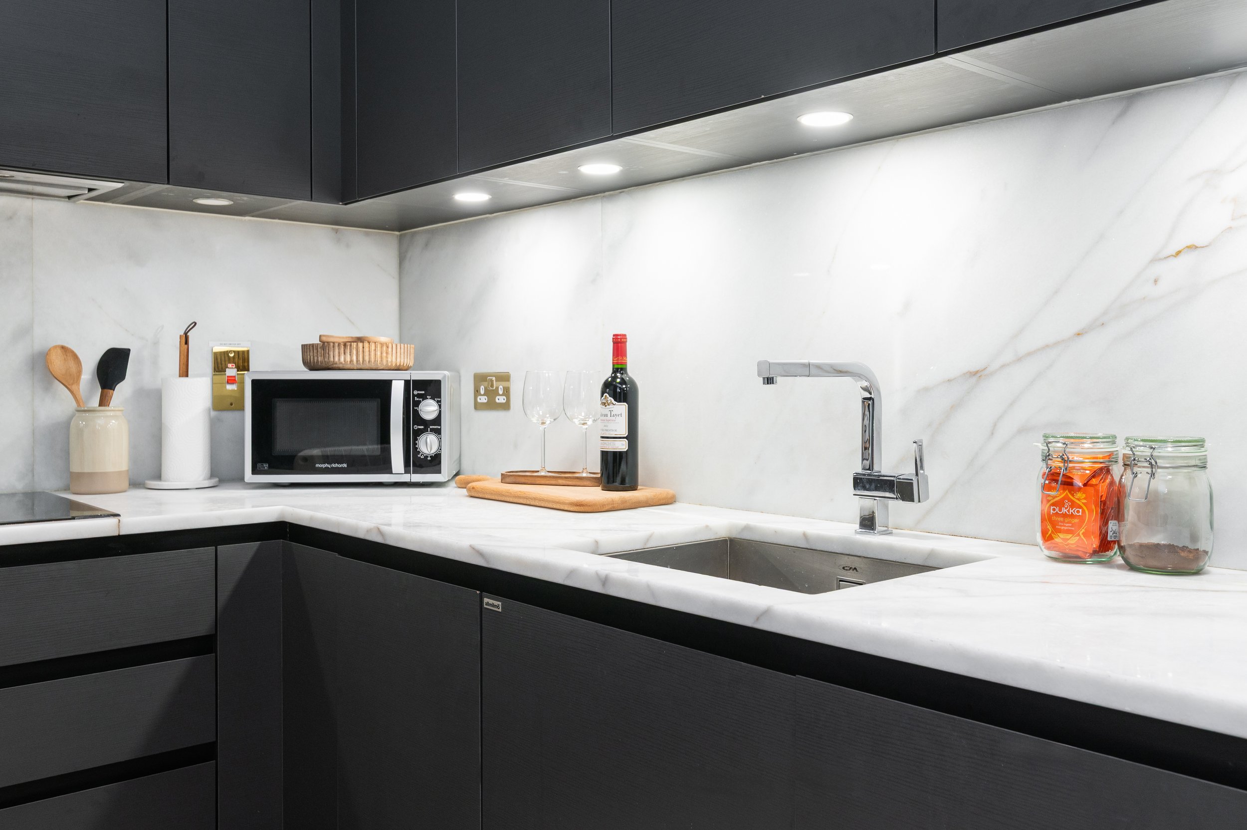 Modern kitchen with black cabinets, white marble countertops and backsplash, stainless steel appliances including microwave and sink with chrome faucet.