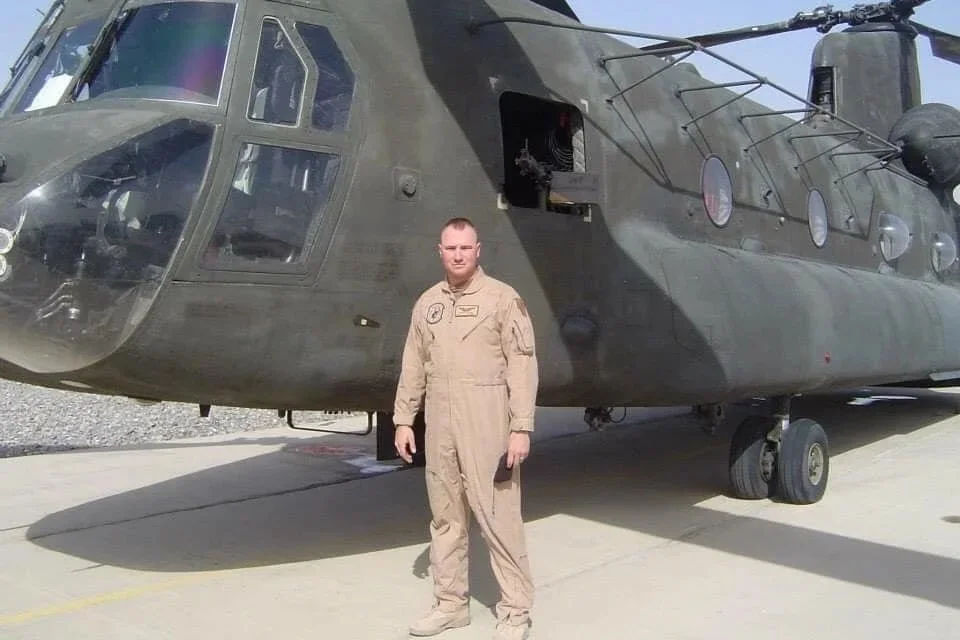 A person in military uniform standing in front of a military helicopter on a concrete tarmac.