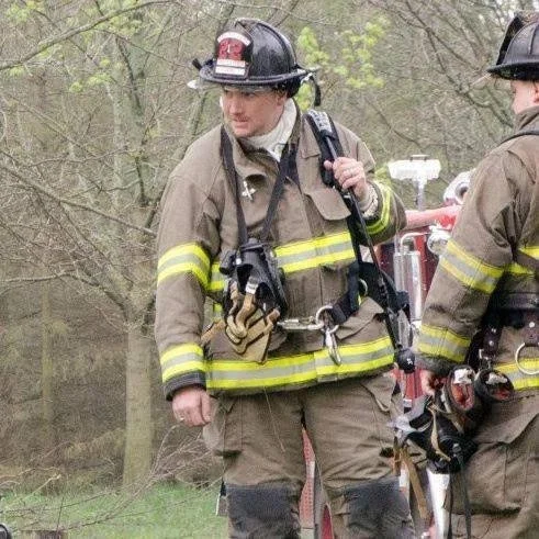Firefighters wearing helmets and gear in an outdoor setting with trees in the background.