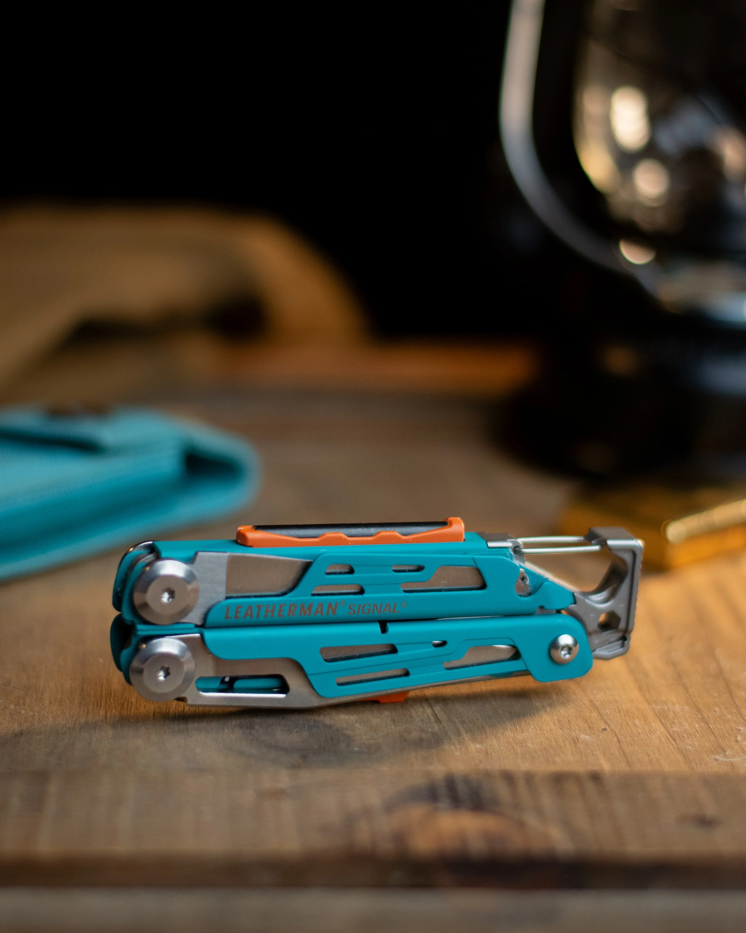 Close-up of a blue and gray leatherman signal multi-tool on a wooden surface with blurred coins and a blue strap in the background.