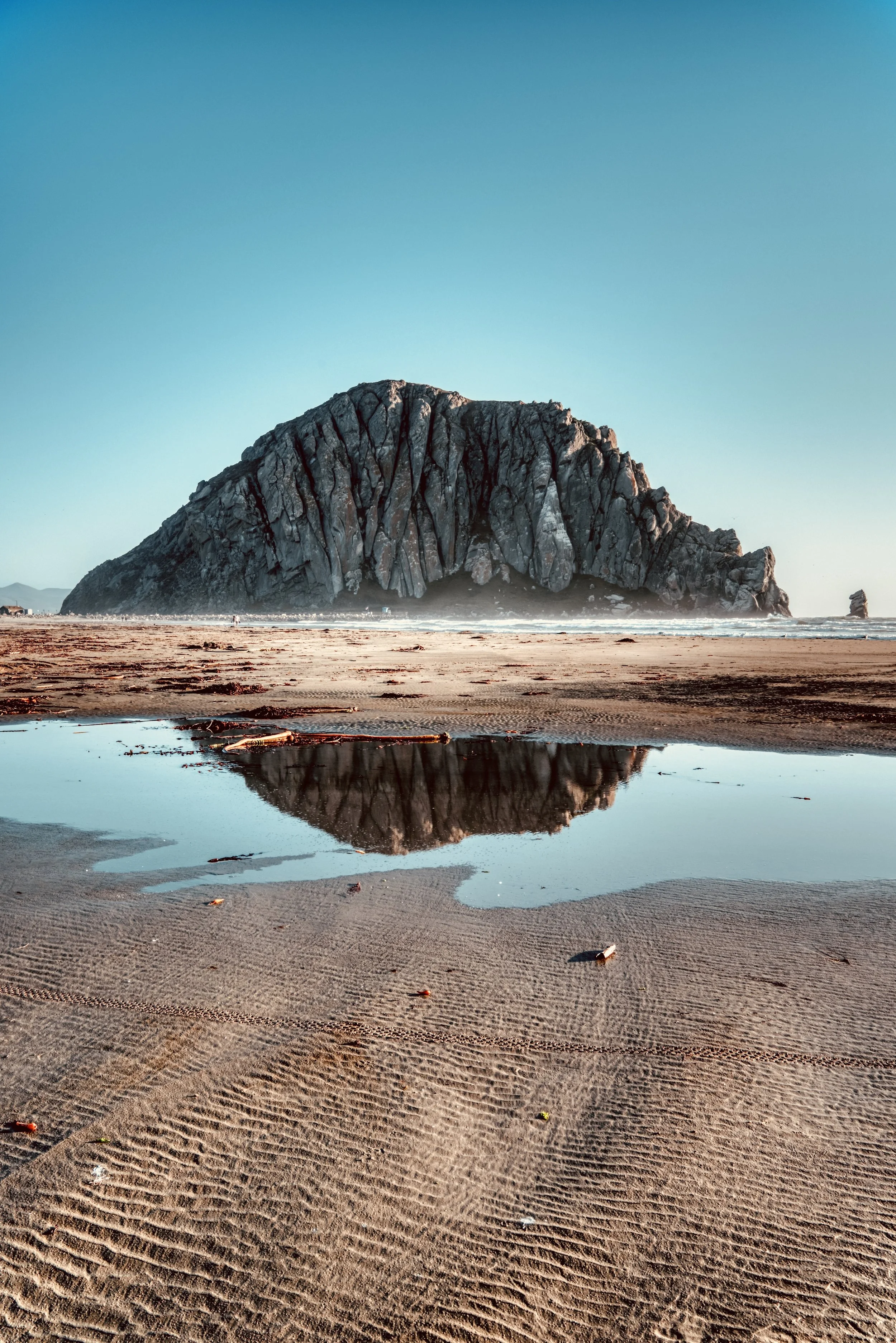Rocky island reflected in a shallow tide pool on a sandy beach under a clear blue sky, captured by Terra Australis Visuals. Coastal landscape photography in Western Australia.