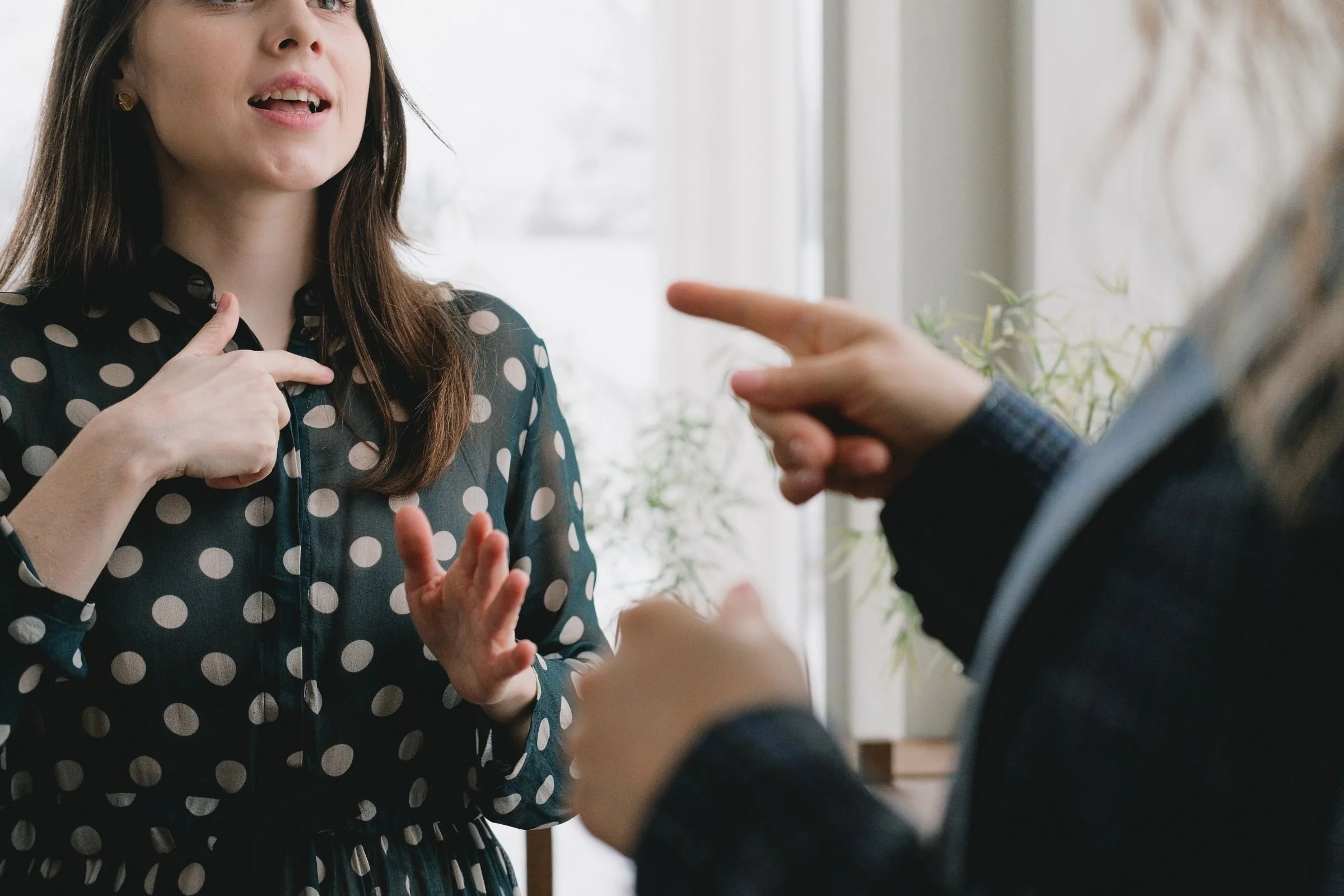 Two people in an expressive argument during a conflict resolution exercise, with one person pointing a finger while the other gestures toward her chest.