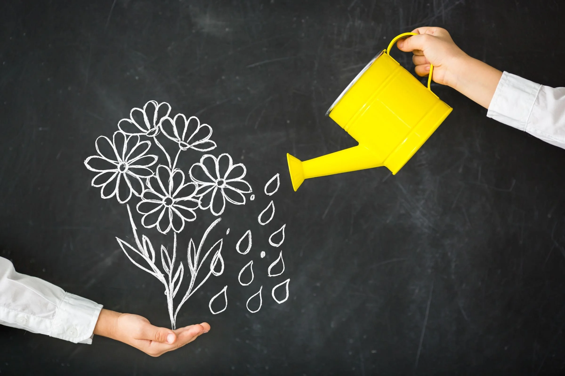 Two hands in white sleeves hold a bright yellow watering can above a chalkboard where someone has drawn flowers and water droplets, illustrating the concept of a growth mindset.