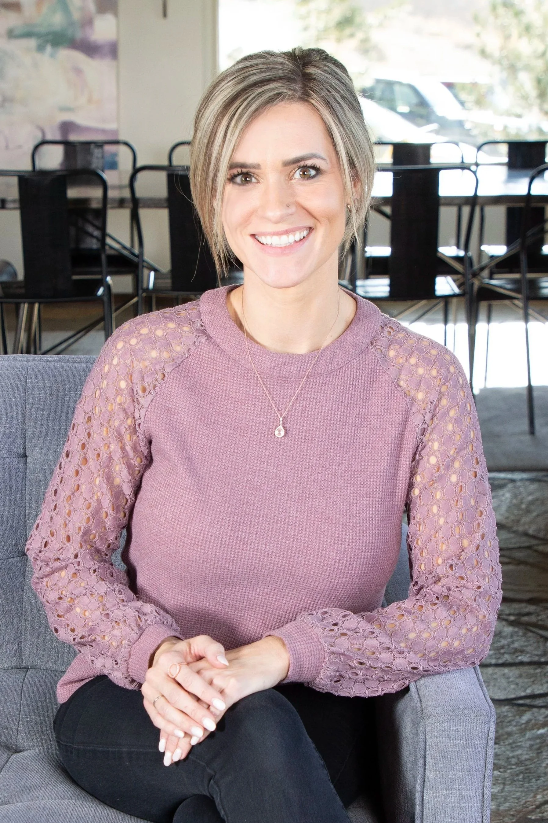 Portrait of a smiling staff member seated on a gray couch in a bright common area.