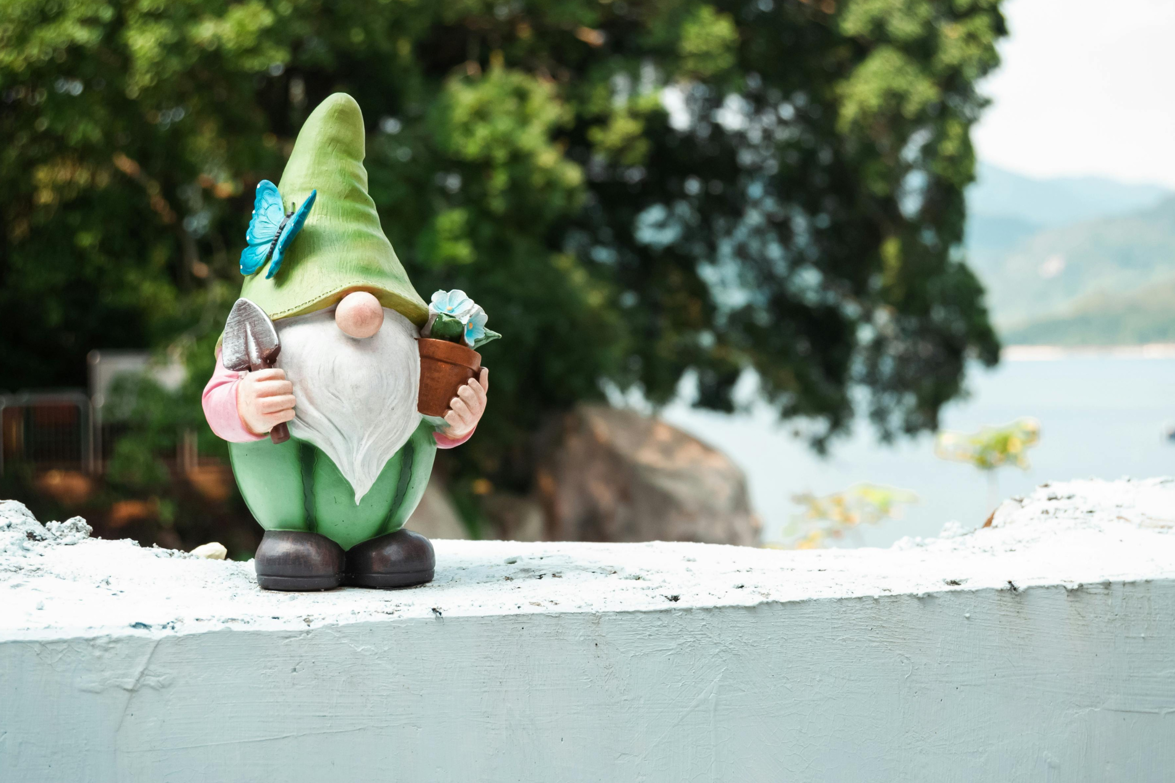 A whimsical gnome statue adorned with a green hat and matching green beard, placed outdoors.