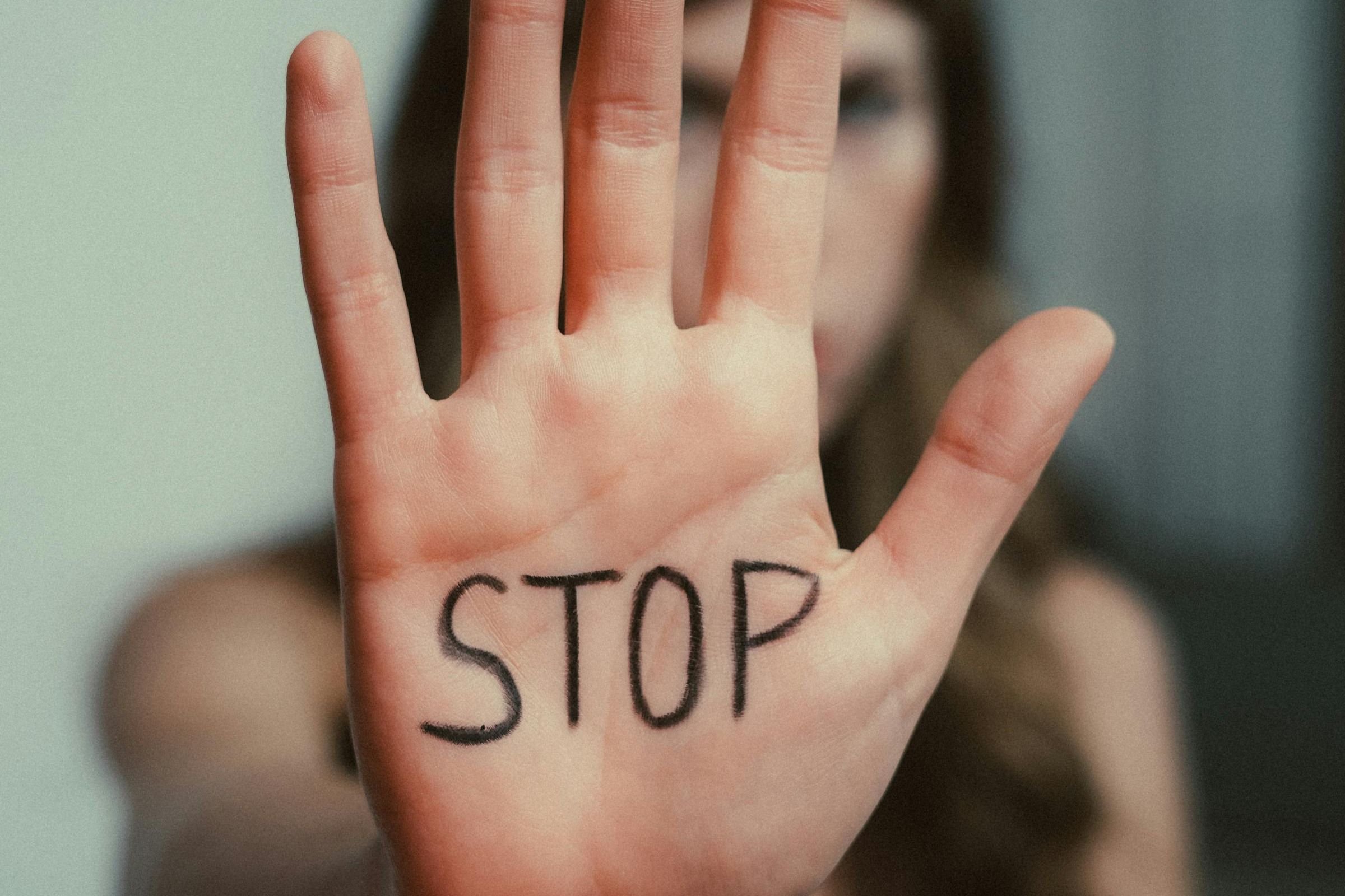 A close-up of a person's hand with "STOP" written on the palm. The background is blurred, emphasizing the hand's clear message and assertive tone.