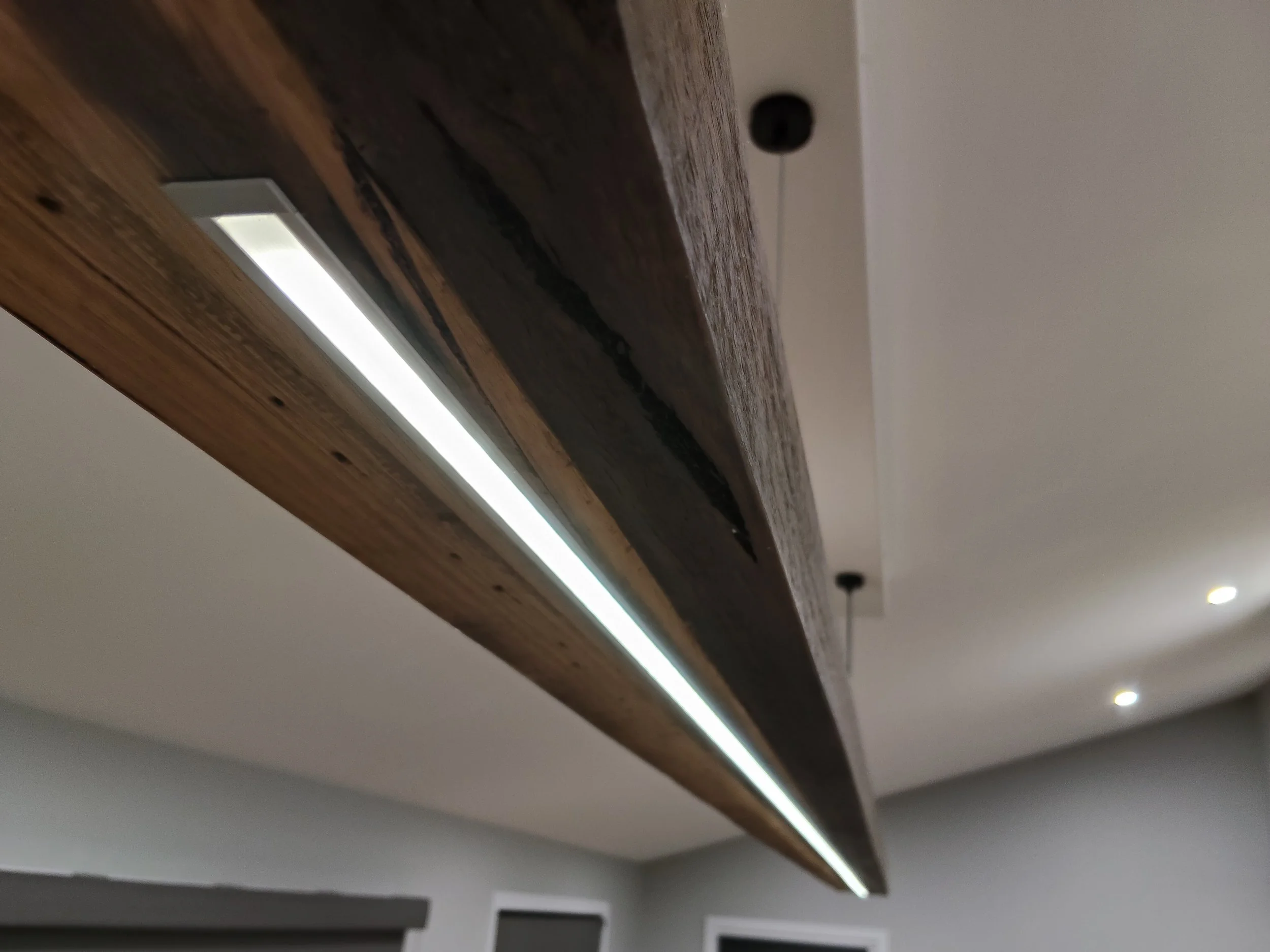 Close-up of a timber ceiling beam with LED strip lighting installed along the bottom edge, hanging from ceiling.