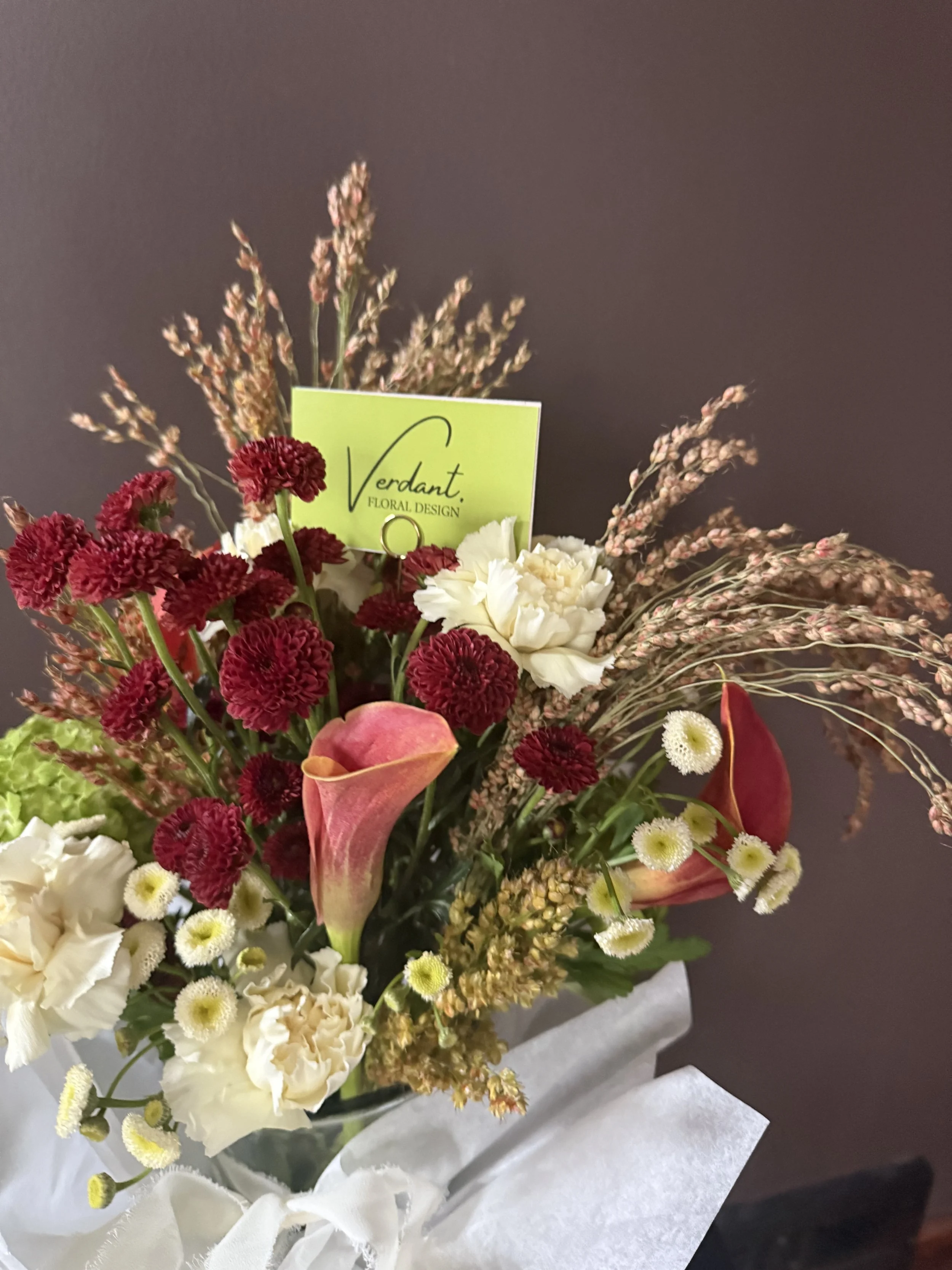 Colorful floral bouquet with calla lilies, carnations, and other flowers wrapped in white tissue paper.