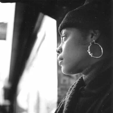 American hip-hop artist T-Love wearing a hoop earring, looking out a window.