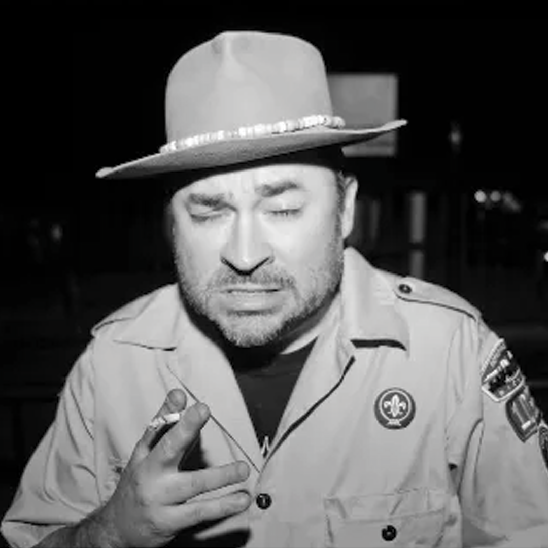 Canadian indie artist Spookey Ruben with a beard wearing a scout leader uniform, hat, and smoking a cigar.