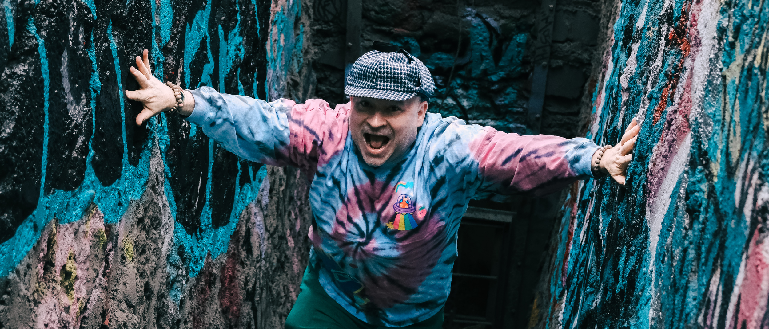 Canadian indie artist Spookey Ruben climbing a graffiti-covered wall, with his mouth open in excitement.