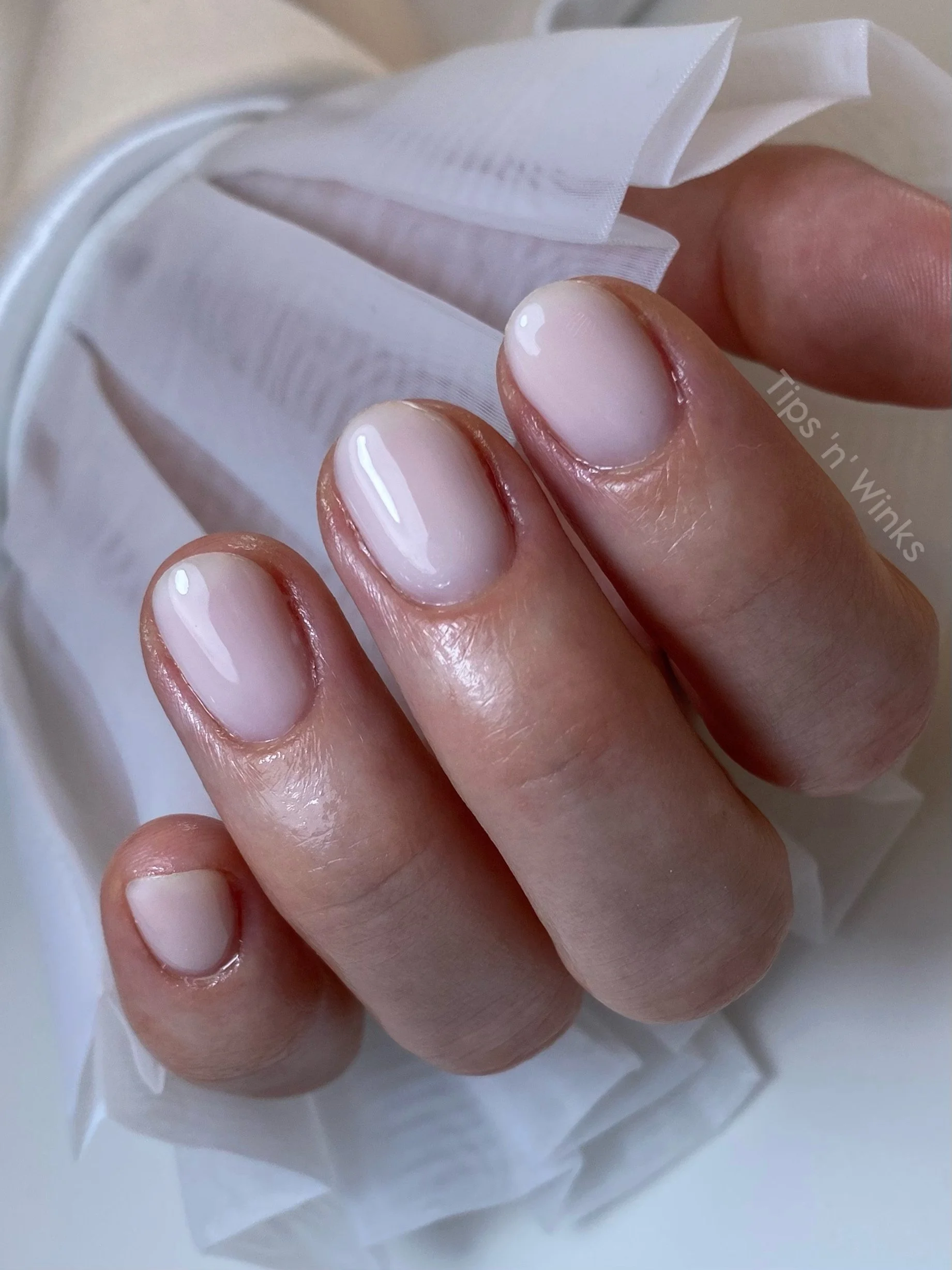 Close-up of a hand with freshly manicured nails in a natural, glossy pink shade.