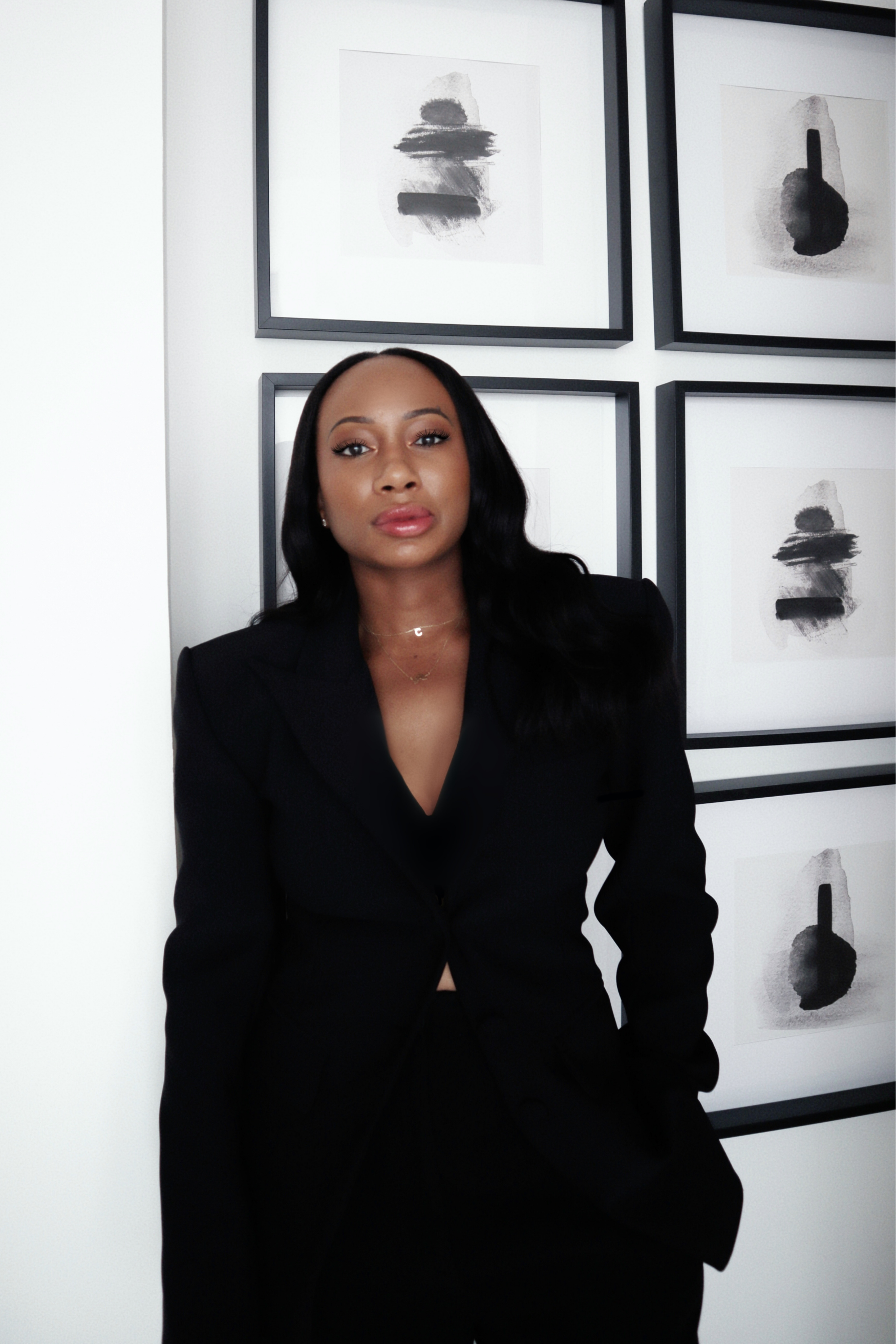Founder of cuhlm Cathy Chakauya wearing a black blazer with long black hair, standing in front of abstract black and white artwork on the wall.