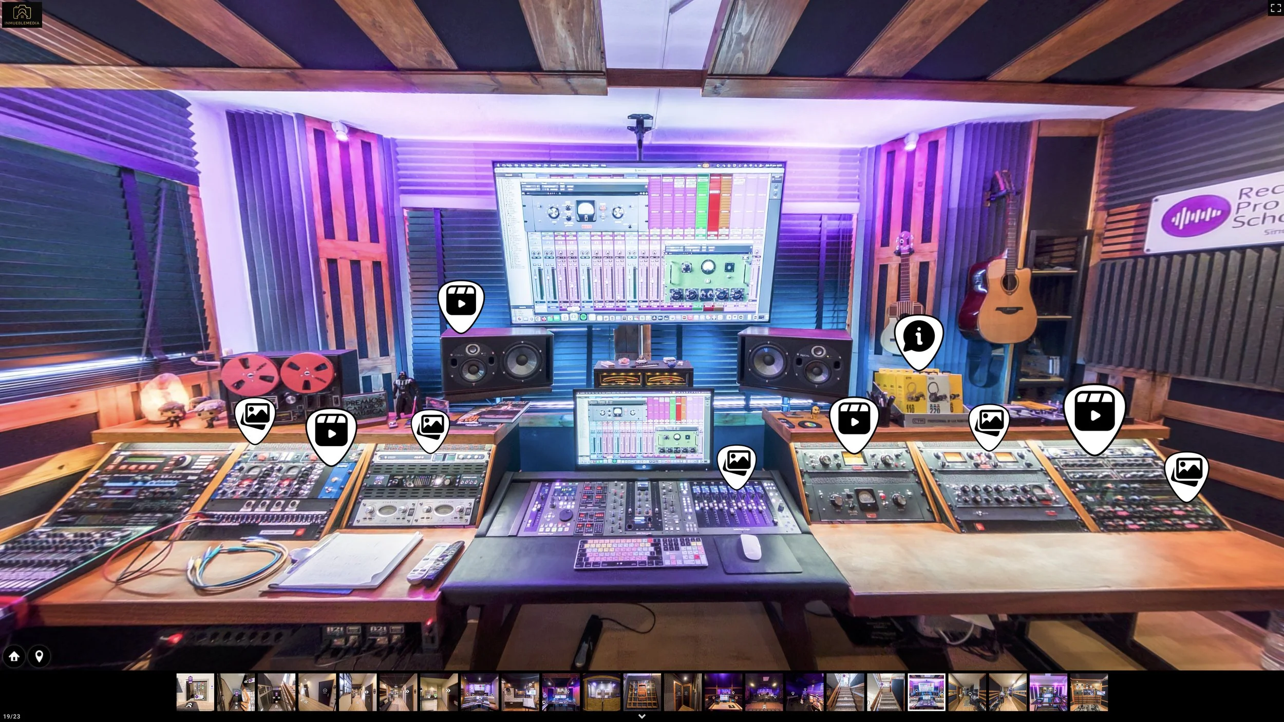 Inside a professional music recording studio with mixing consoles, speakers, guitars, and a large screen displaying music production software.