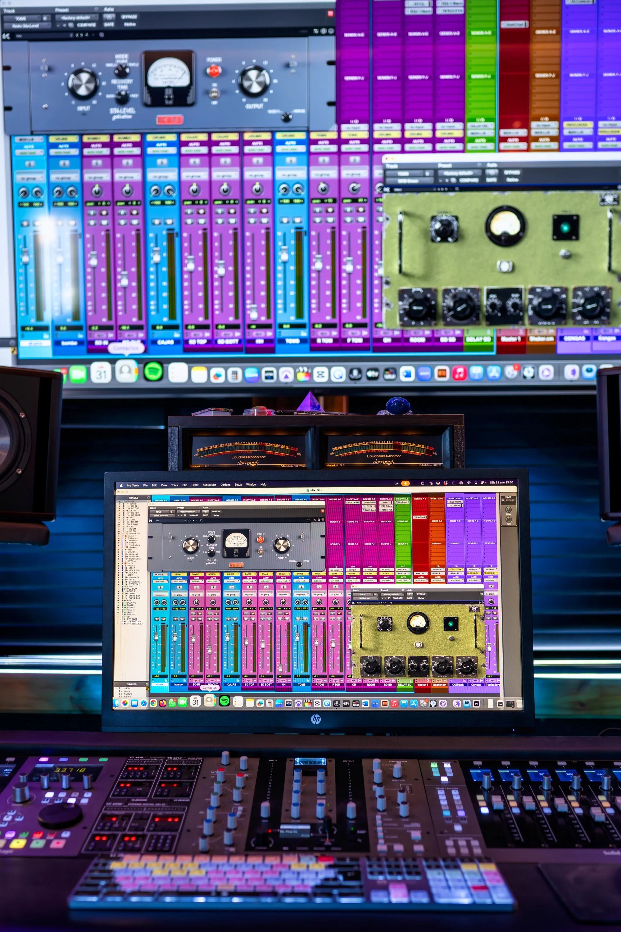 Estación de producción de audio con consolas, monitores con software de grabación y mezcla, y pantallas con interfaz de audio y archivo de mezcla.