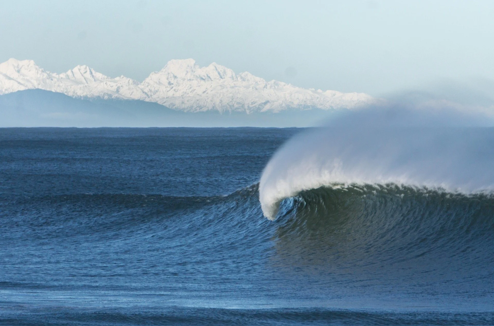 Ocean wave with snowy mountains in the background.
