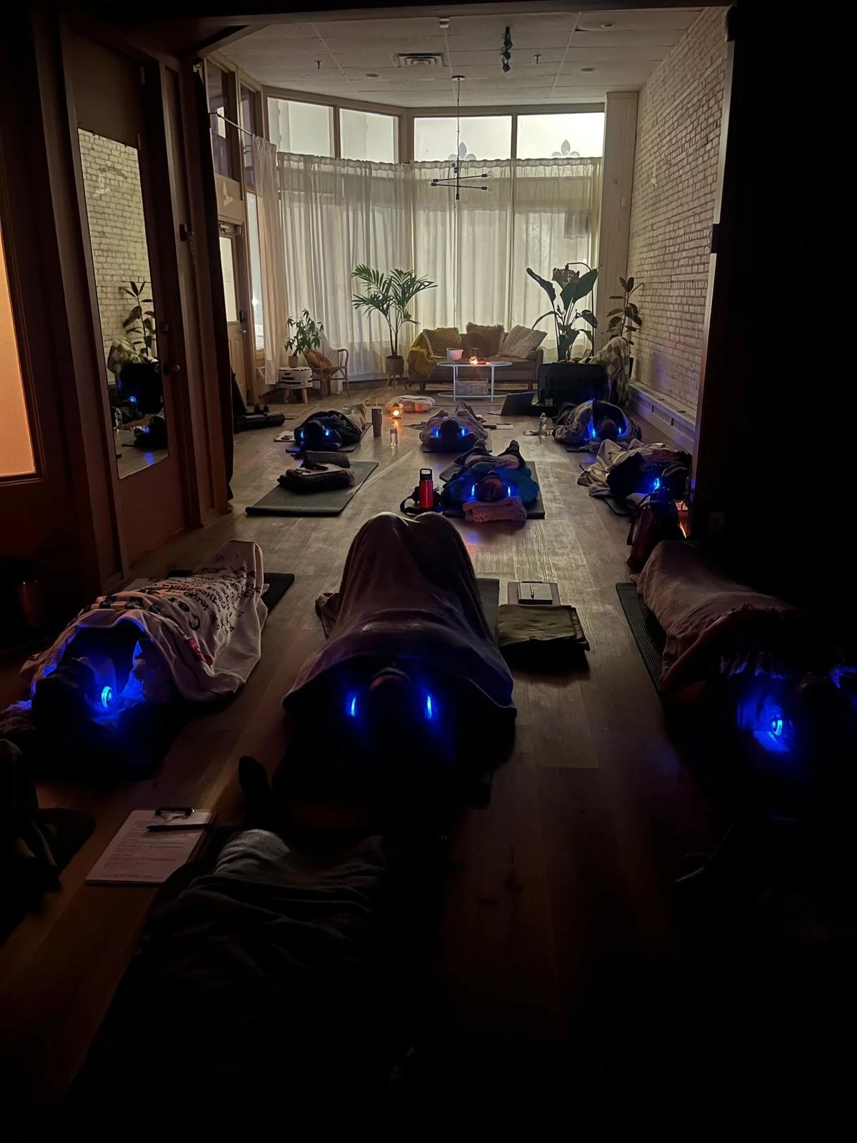 eight people laying on yoga mats with blankets and headphones in a cozy space doing breathwork