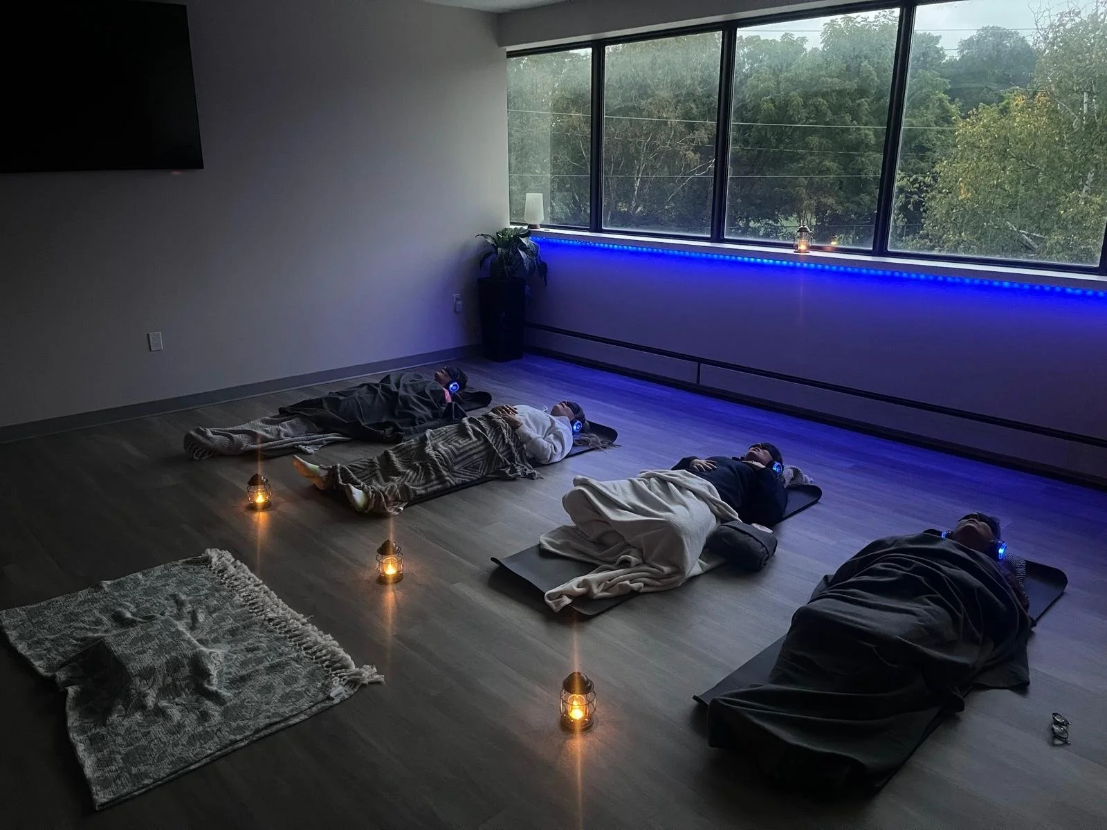 four people laying on mats in a cozy spacious room with headphones on doing breathwork