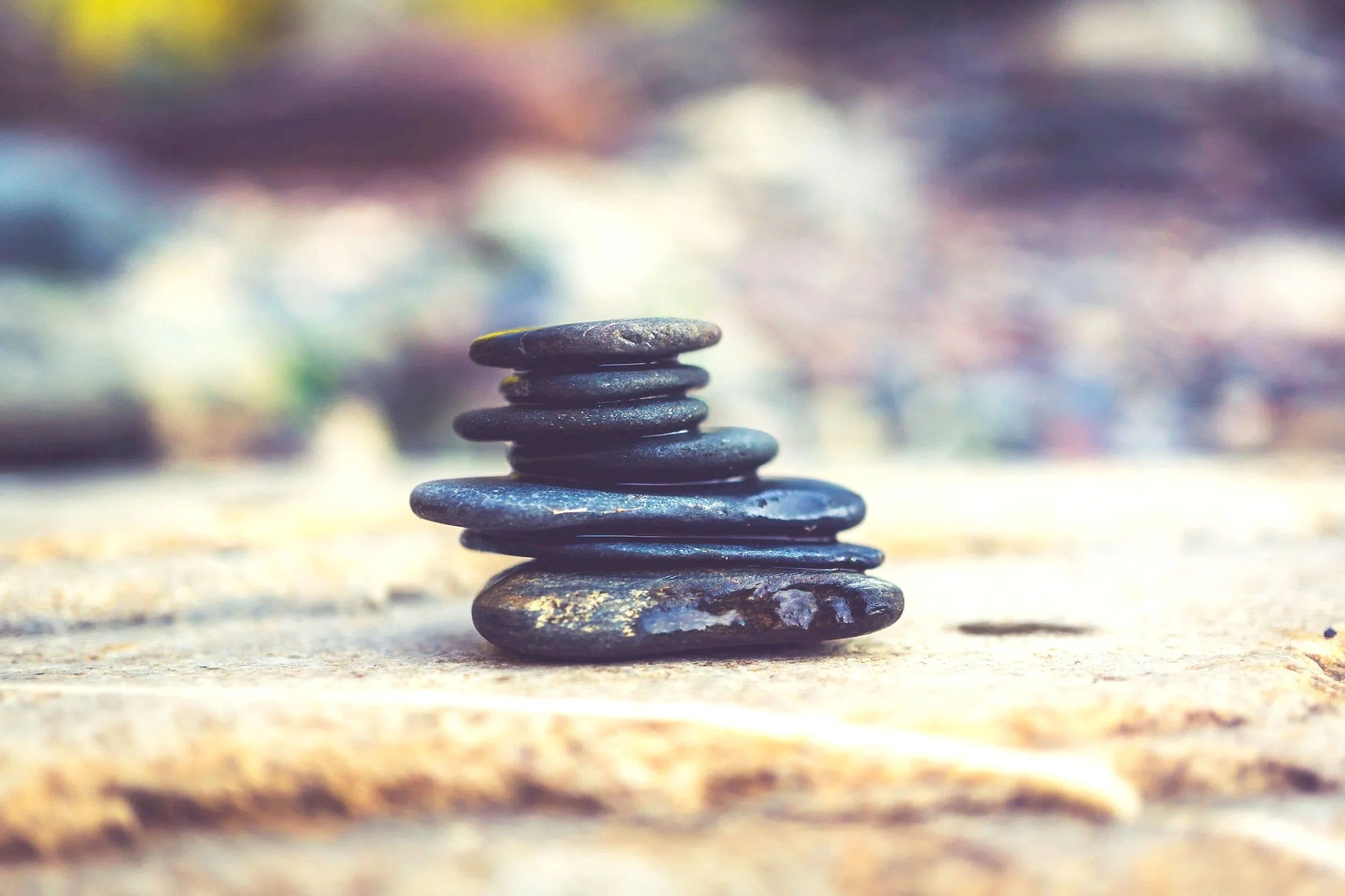 Stack of smooth black stones arranged on a wooden surface with a blurred background.