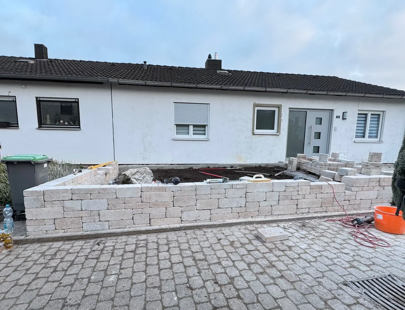 Baustelle vor einem weißen Haus mit einem halb fertig gemauerten Bereich aus Ziegelsteinen.