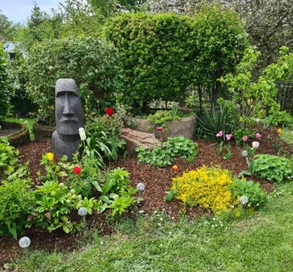 Garten mit Moai-Statue, verschiedenen Blumen und Sträuchern