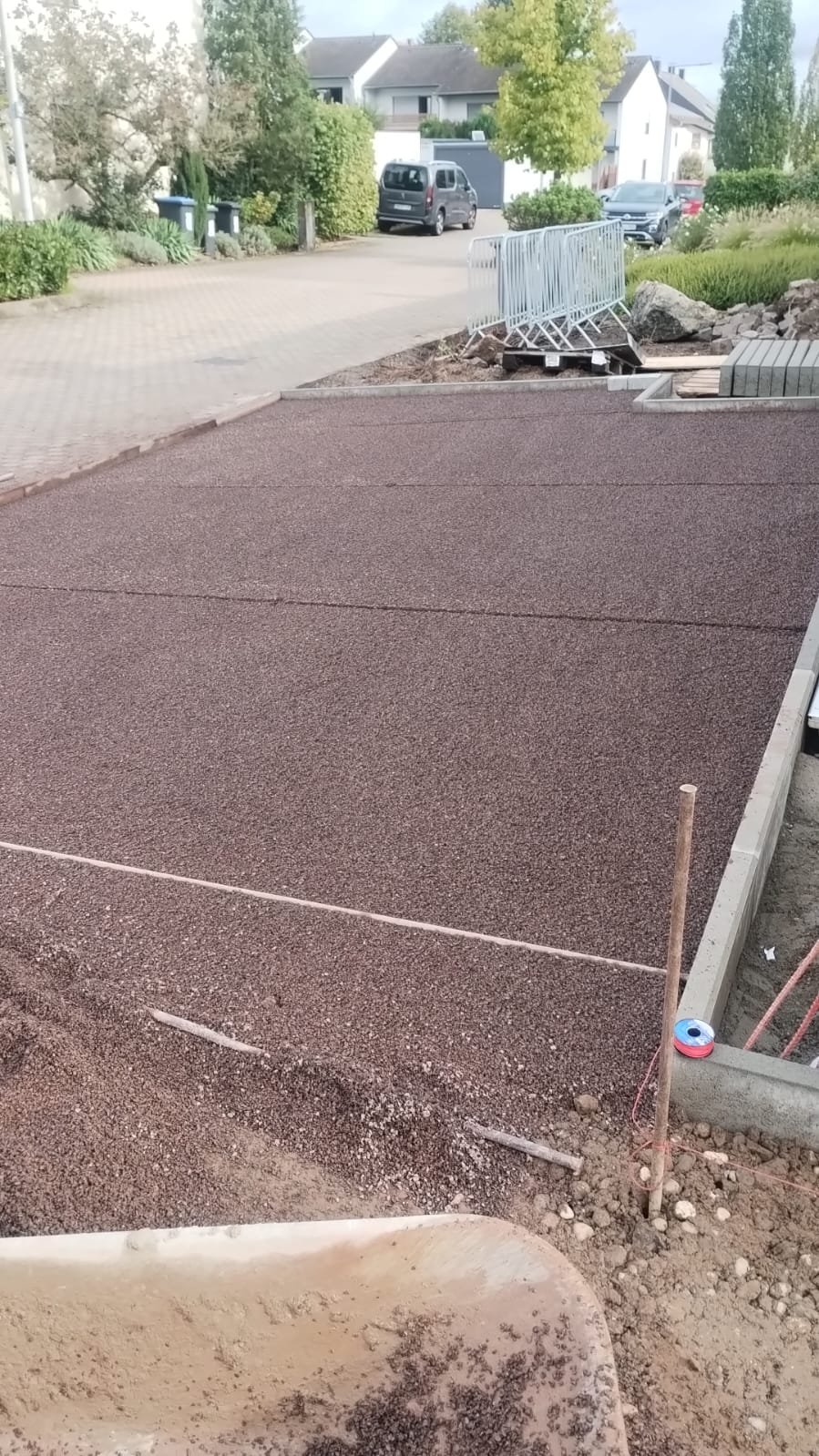 Neue gepflasterte Fläche vor einem Haus, im Hintergrund sind Zäune, Fahrzeuge und Bäume. Es sieht nach einem Bauprojekt aus.