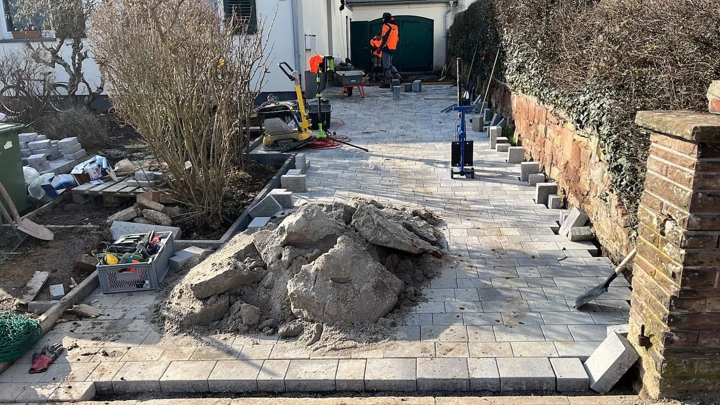 Modernes Gartenweg- und Terrassenpflasterungsprojekt im Bau, mit Steinen, Werkzeugen und Bauarbeiten.