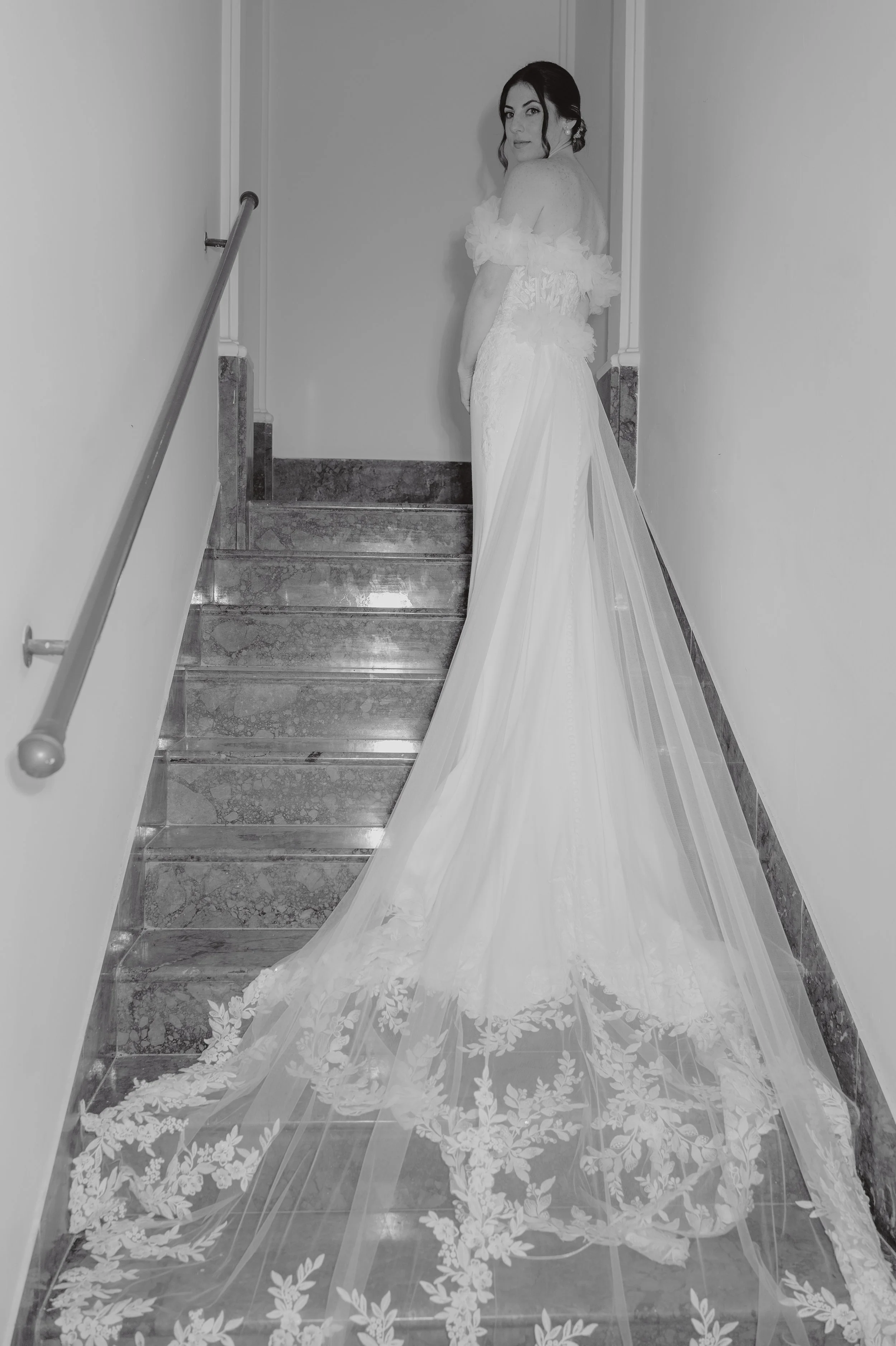 A woman in a wedding dress standing on a staircase, looking back over her shoulder.