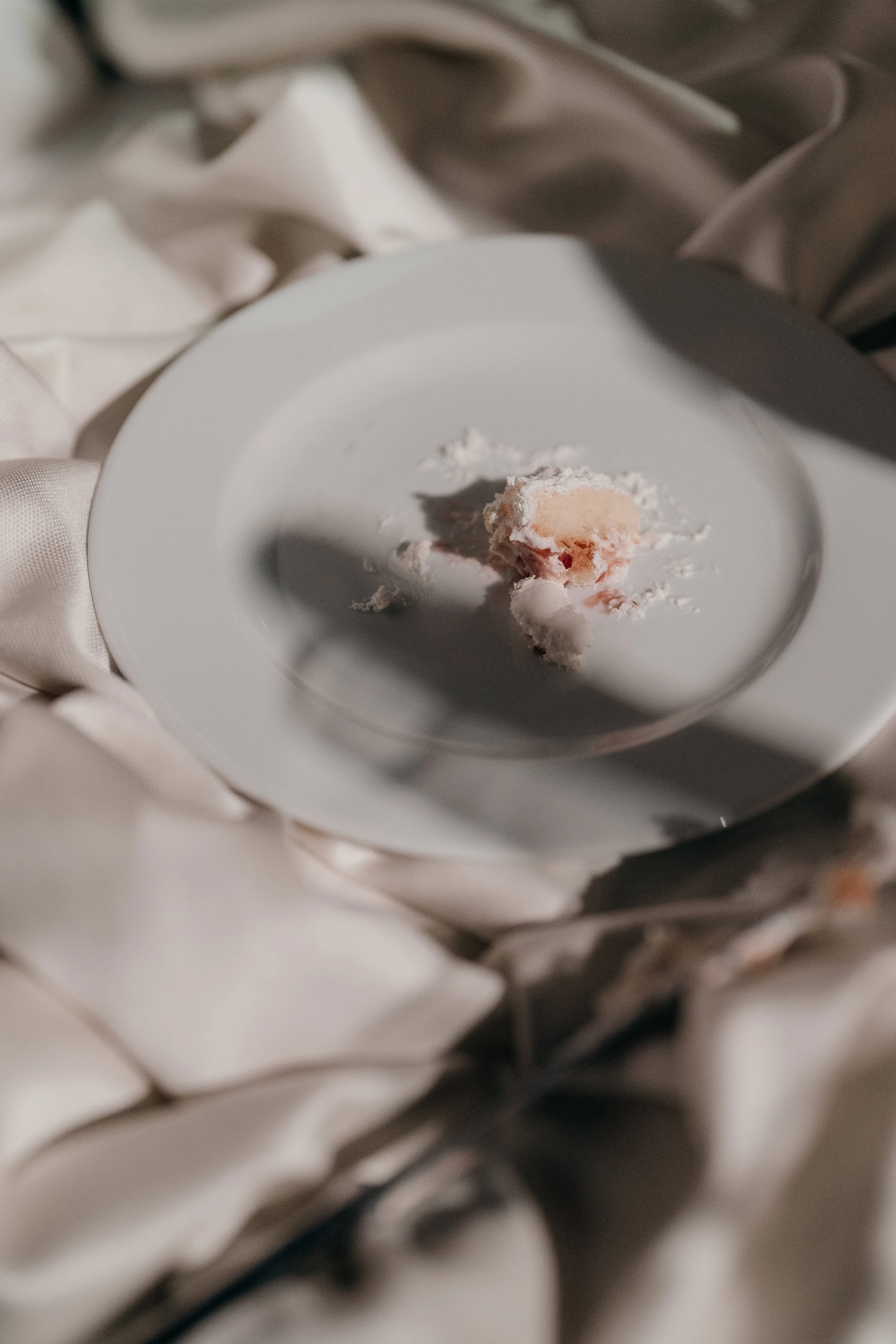 A white plate with a partially eaten pink and white dessert on it, placed on a satin-like fabric.