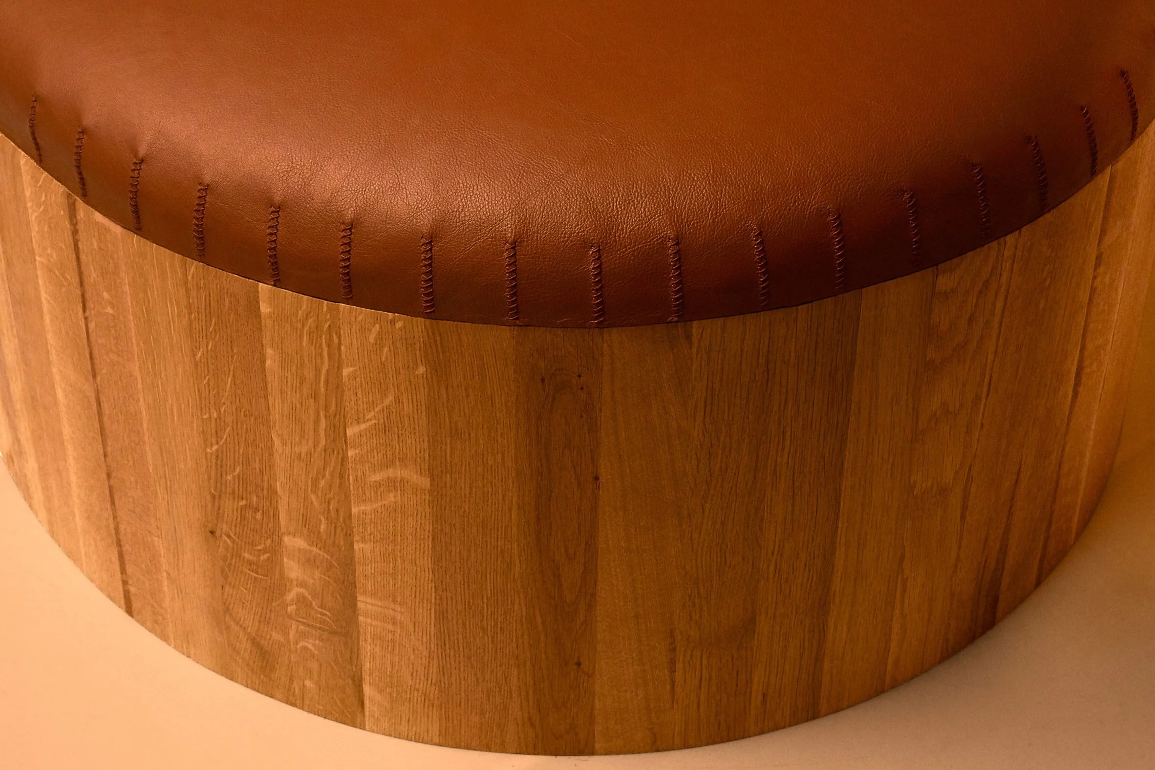 Close-up of the hand-stitched perimeter on a natural leather surface of a Joe Doucet Columns bench.