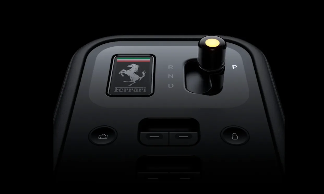 Close-up view of the minimalist, high-tech black key fob for the Ferrari Luce, featuring a digital E Ink Prancing Horse badge with an Italian flag accent and a physical gear selector pin showing a glowing yellow light indicator.