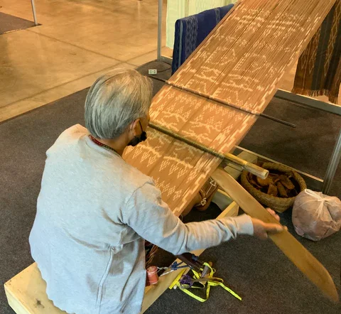 An artisan weaver working at a traditional wooden loom, demonstrating the human craft and meaningful action that creates true value in Post-Luxury objects.