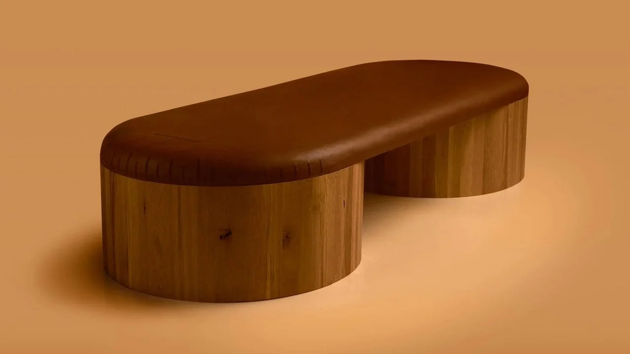 A sculptural bench from Joe Doucet’s Columns collection featuring two massive cylindrical solid oak bases joined by a continuous surface of rich brown natural leather.