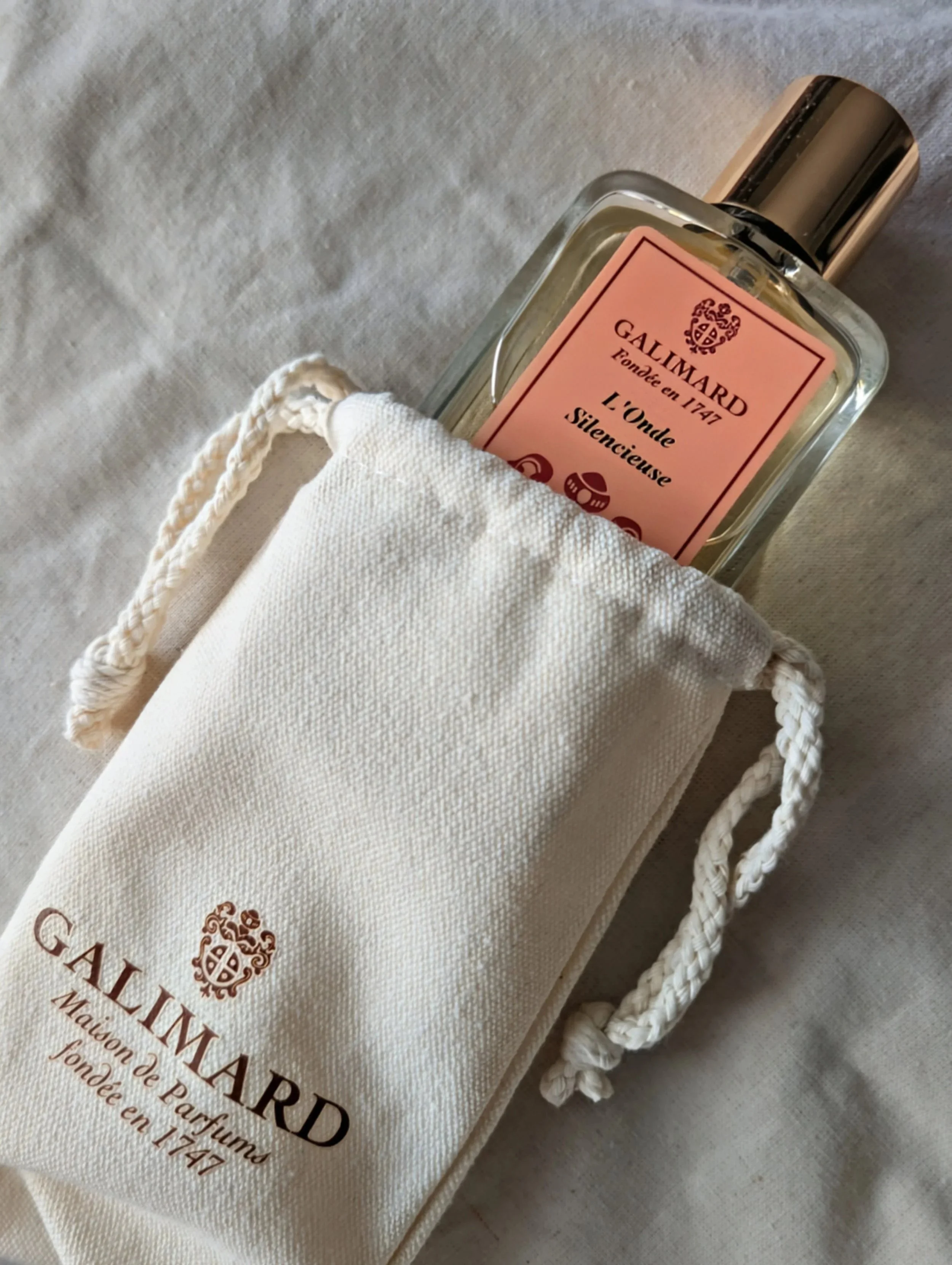 The 100ml bottle of L’Onde Silencieuse Extrait de Parfum resting inside a branded Galimard canvas pouch on a linen background.