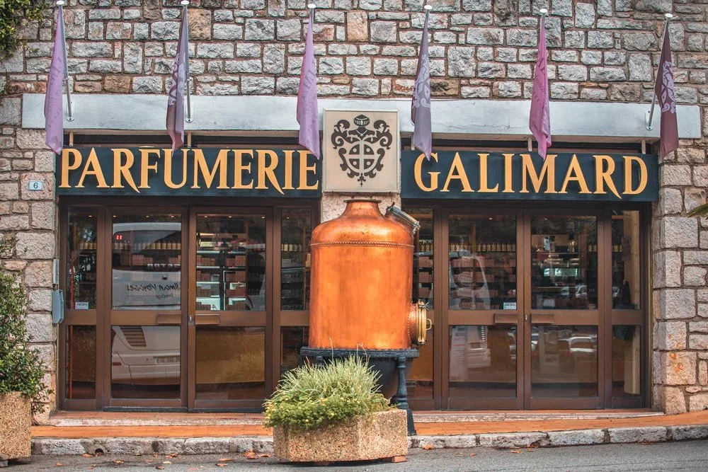 The stone-walled exterior of Parfumerie Galimard featuring a large copper distillation still and traditional signage.