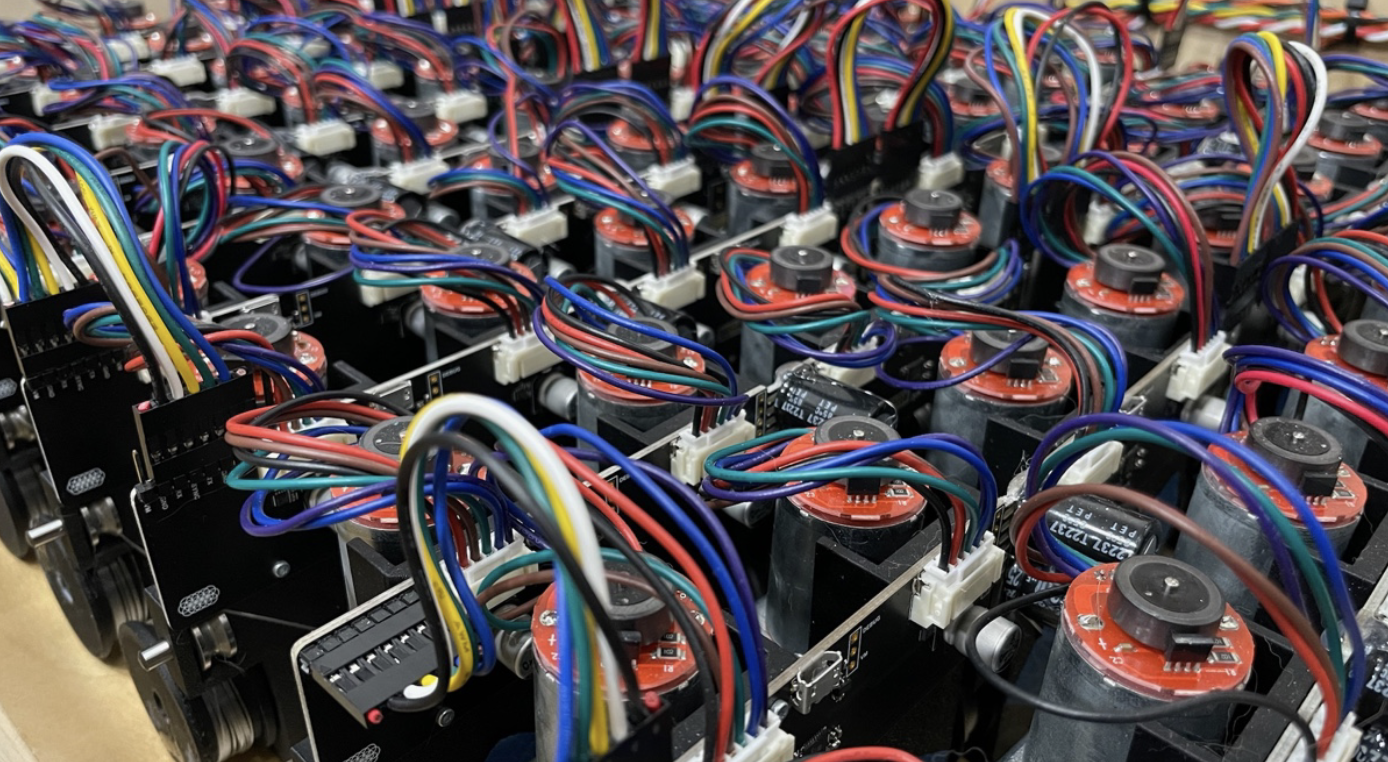 A dense, organized grid array of micro mechanical stepping actuators and compact electric motors with intricate, neatly routed bundles of multicolored wiring harnesses connected to black circuit boards.