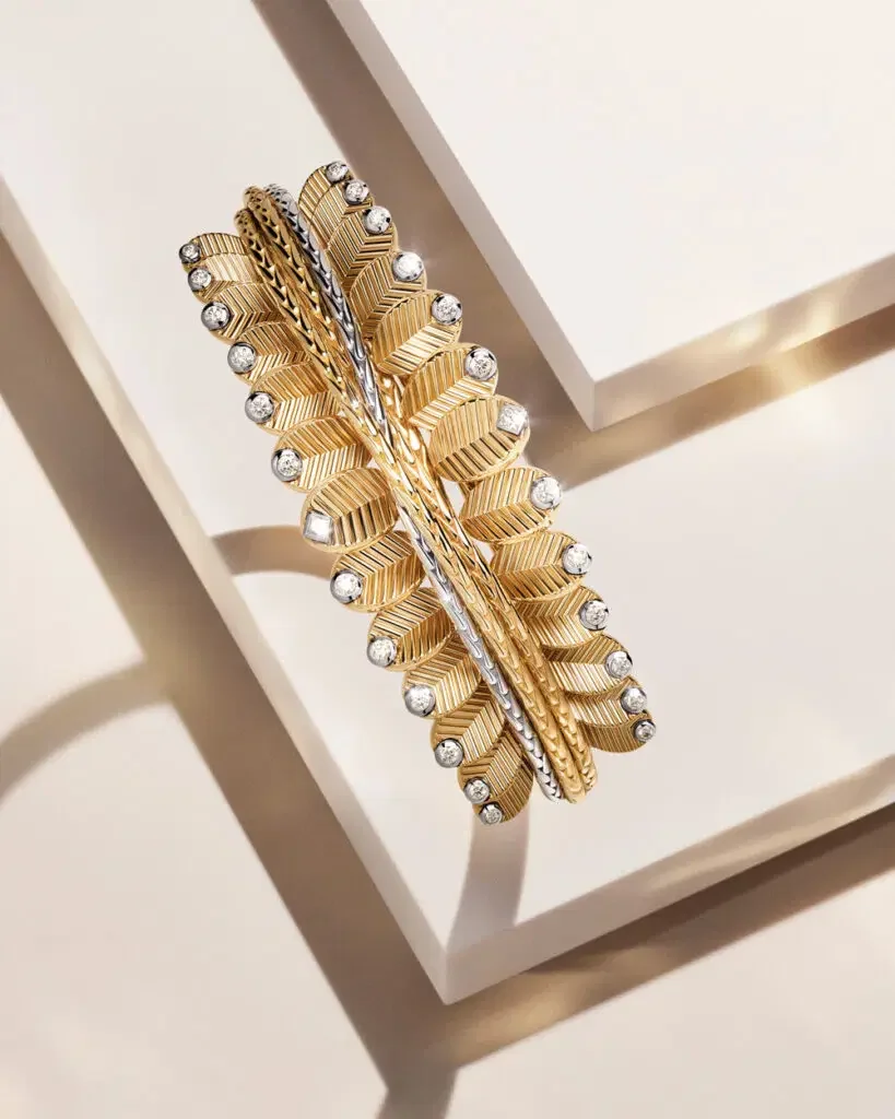 A high-end studio shot of a Cartier Grain de Café ring, featuring repeating yellow gold coffee-bean motifs with ribbed textures and diamond accents, displayed on minimalist geometric pedestals.
