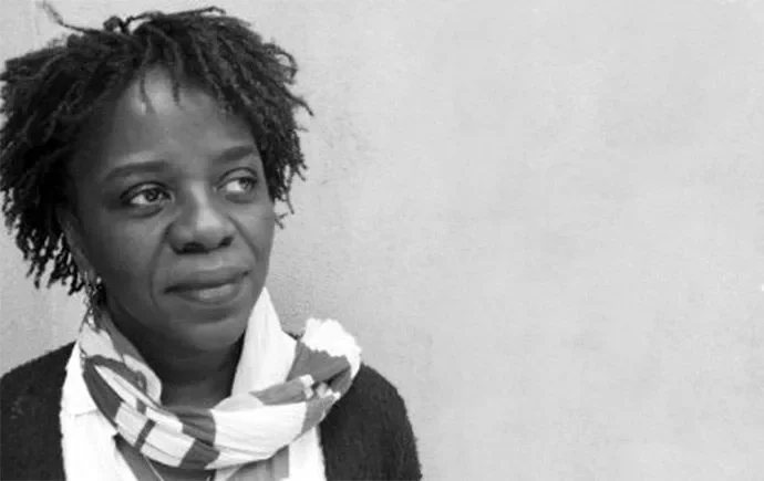 A high-quality black and white portrait of Denise Ferreira da Silva looking pensive against a textured concrete wall, illustrating her e-flux journal study on the affective architecture of liberal capital.