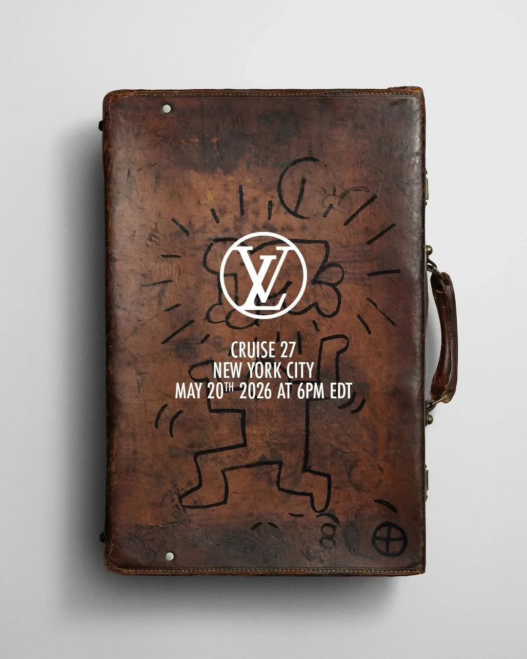 A dark brown leather briefcase with a heavy patina with artwork by Keith Herring drawn on it in black with the Lewis Vuitton cruise 27 logo and information on top of it as a promotional item