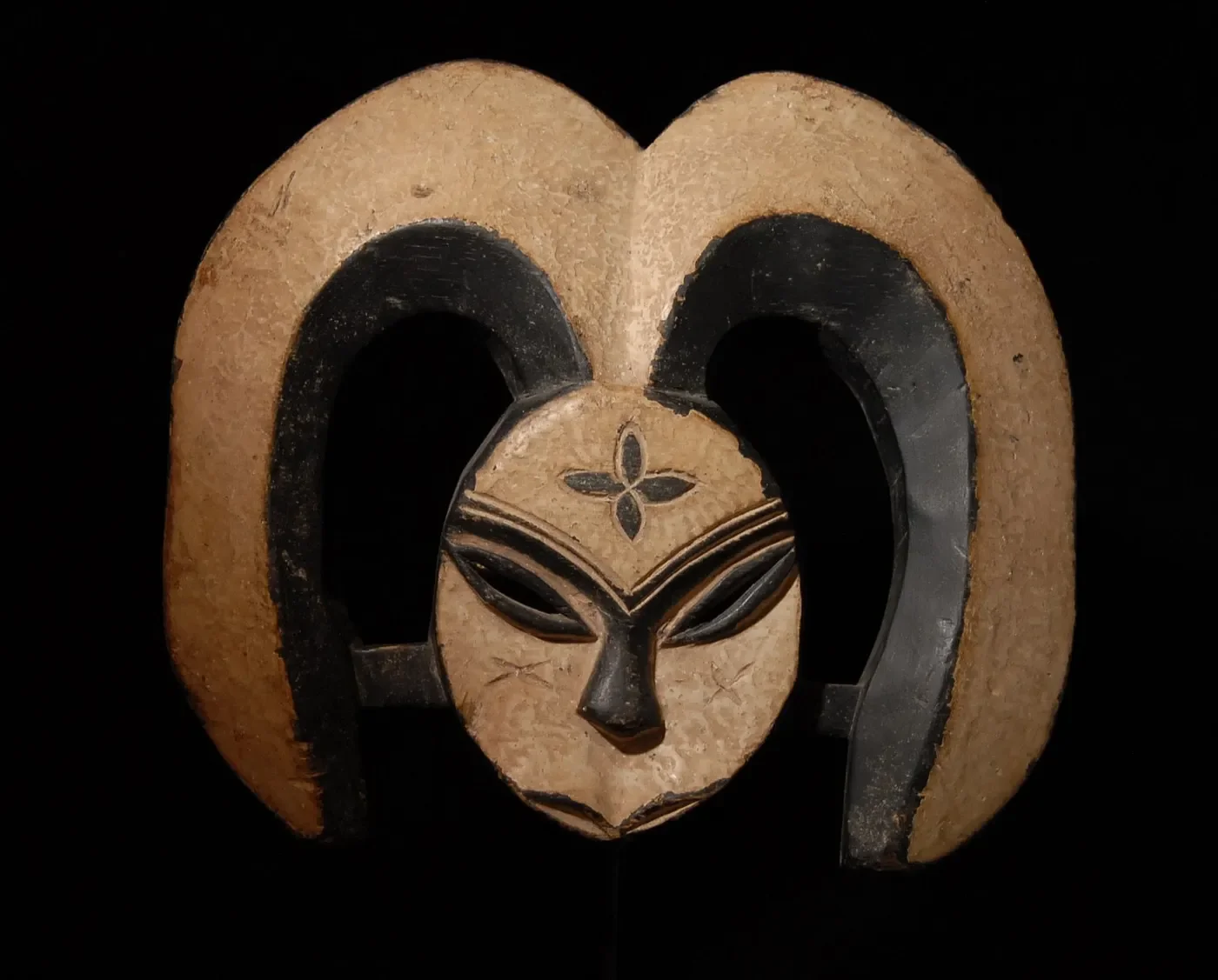 A traditional wood-carved Kwele mask from Gabon featuring a concave heart-shaped face, white kaolin pigment, and downward-curving horns.