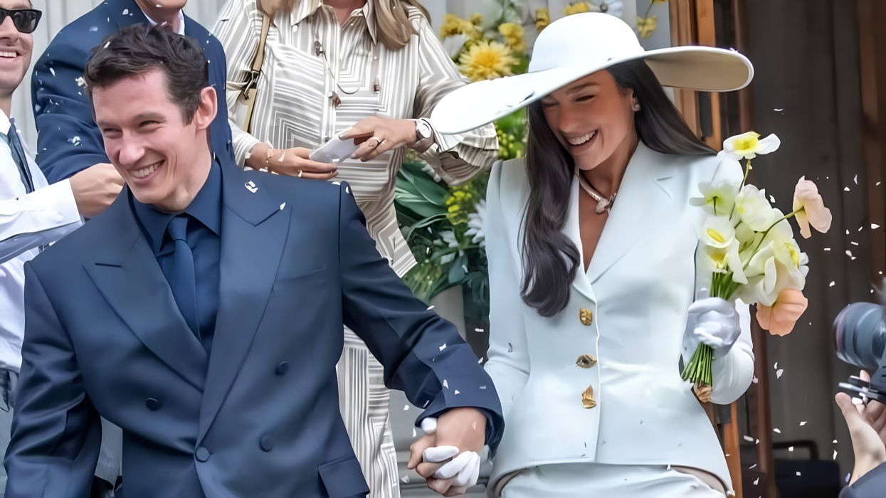 Dua Lipa and Callum Turner outside Old Marylebone Town Hall, with Lipa wearing a custom ivory cady Schiaparelli Haute Couture blazer with gold bijoux buttons, an asymmetric skirt, a Bvlgari Serpenti necklace, and a wide-brimmed Stephen Jones hat.