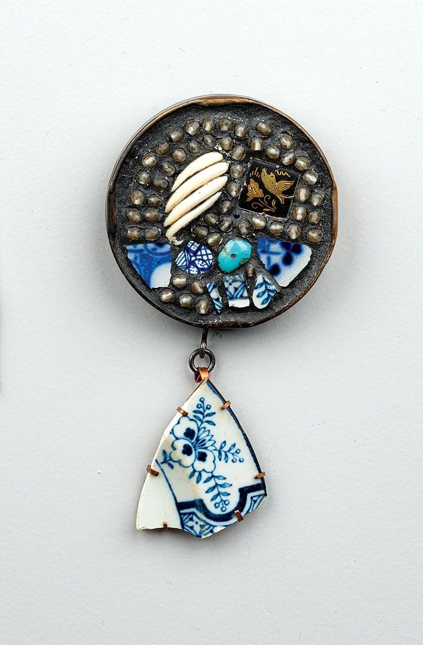 A brooch by artist Robert Ebendorf, created from discarded detritus, including broken blue-and-white porcelain shards, a small shell, and turquoise, set in a dark circular frame.