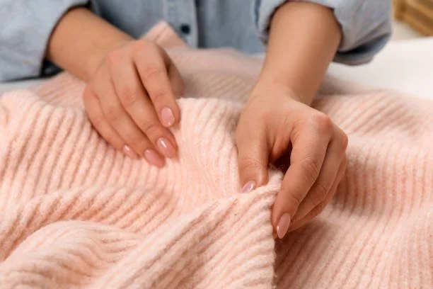 A close-up of a person's hands gently touching the soft, ribbed texture of a pink knit garment, illustrating the concept of haptic memory.